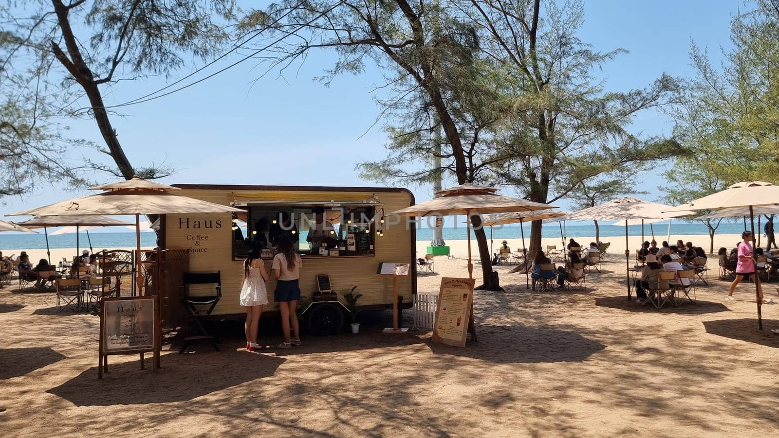 A diverse group of people enjoying freshly prepared food from a bright food truck on a sunny beach by fokkebok