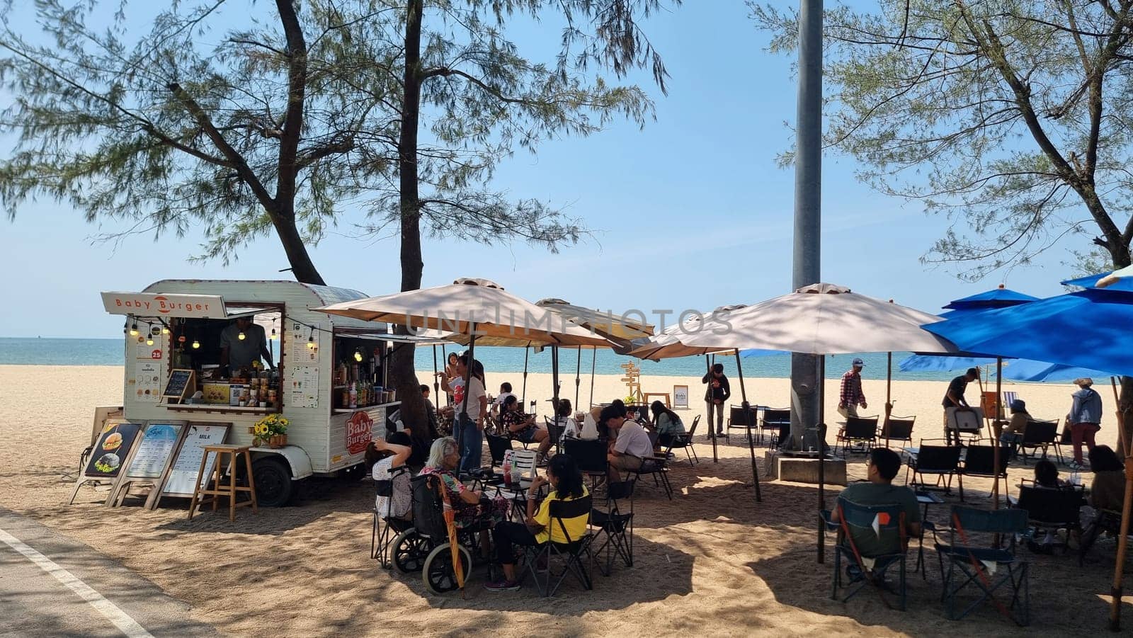 A group of people relaxing under colorful umbrellas on a sandy beach, enjoying the warm sun and scenic ocean views by fokkebok