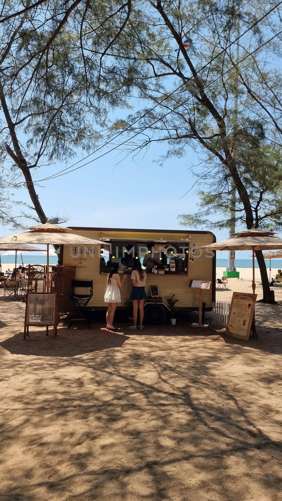 A vibrant food truck is parked on a sandy beach, offering delicious meals to beachgoers on a sunny day by fokkebok