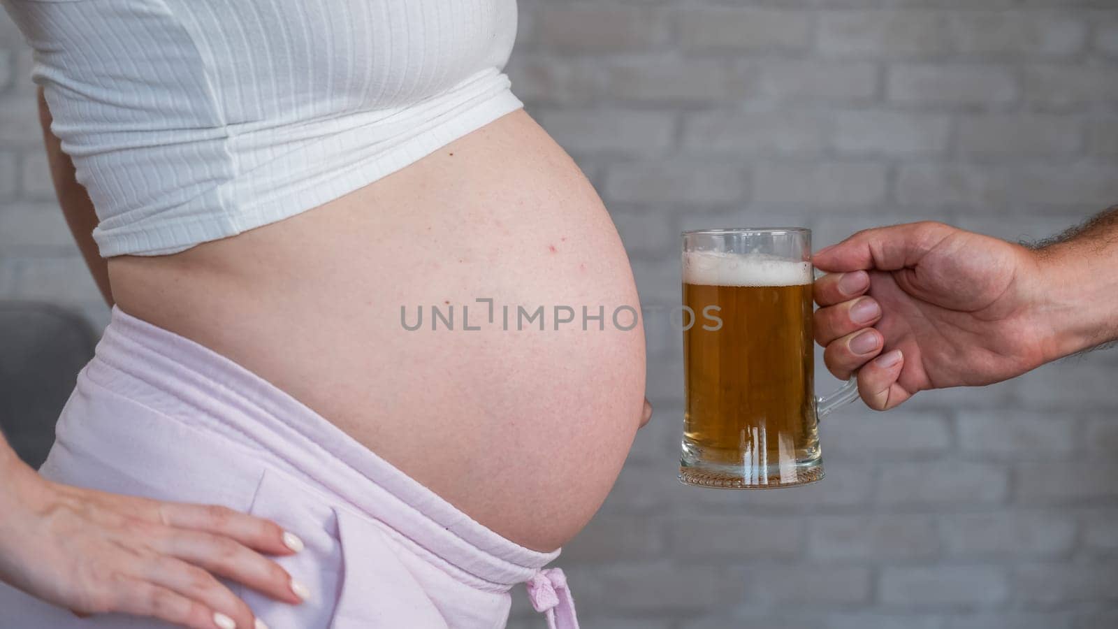 A man clinks a bottle of beer with a pregnant woman's belly. by mrwed54