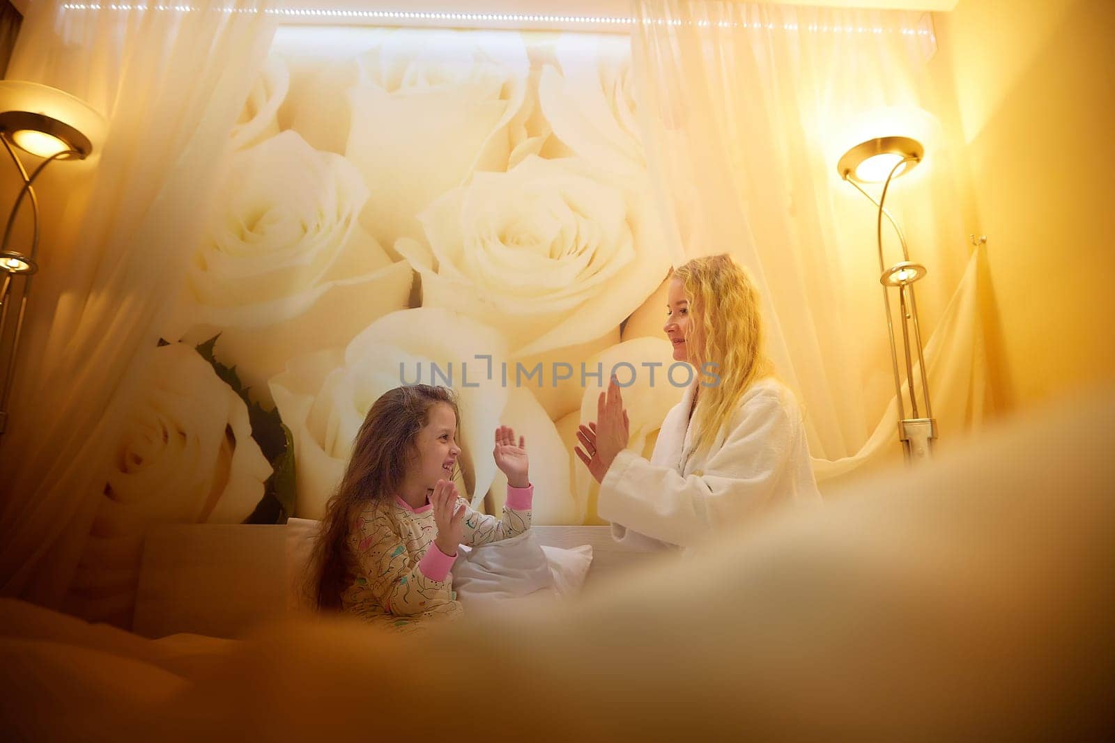 Mother and daughter having relax, fun, play together on bed in bedroom. The concept of tenderness between mom and girl