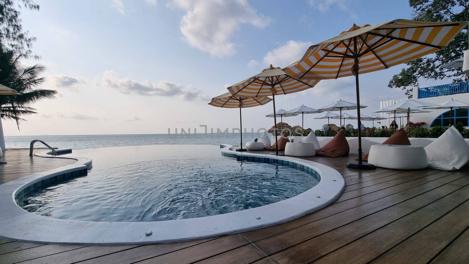 A luxurious, resort-style swimming pool surrounded by palm trees, overlooking a pristine sandy beach and crystal-clear ocean waves by fokkebok