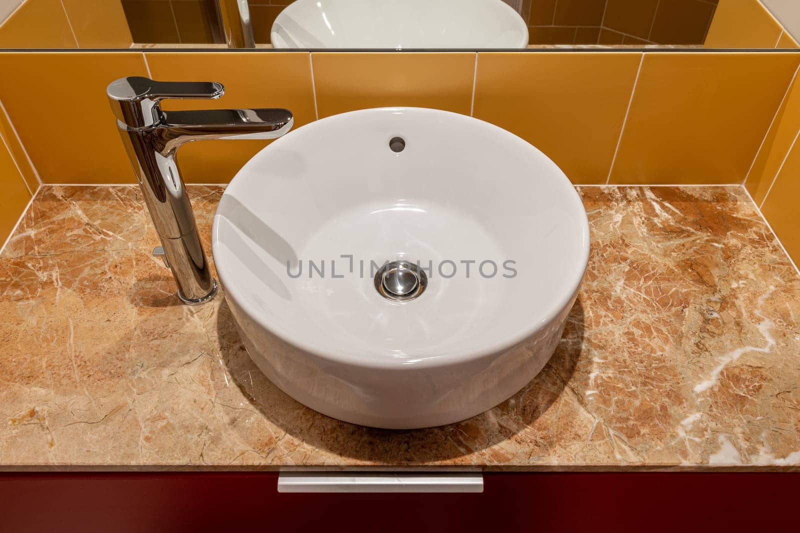 A Bathroom round white Sink With A Faucet And A Mirror.