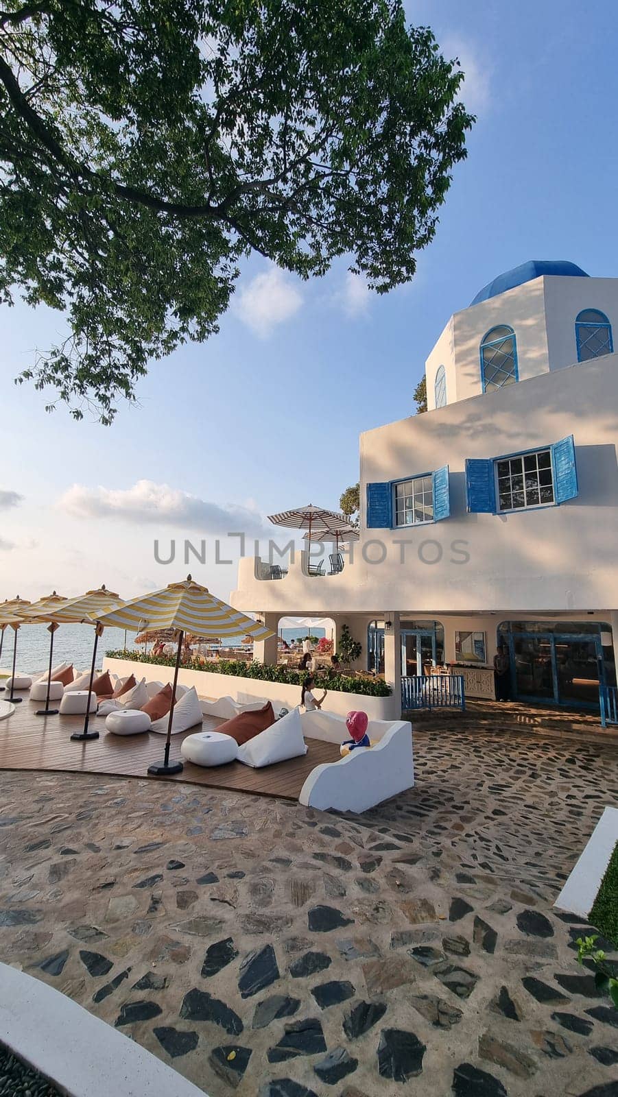 A grand white building adorned with bright blue shutters and umbrellas, standing tall under a clear blue sky by fokkebok