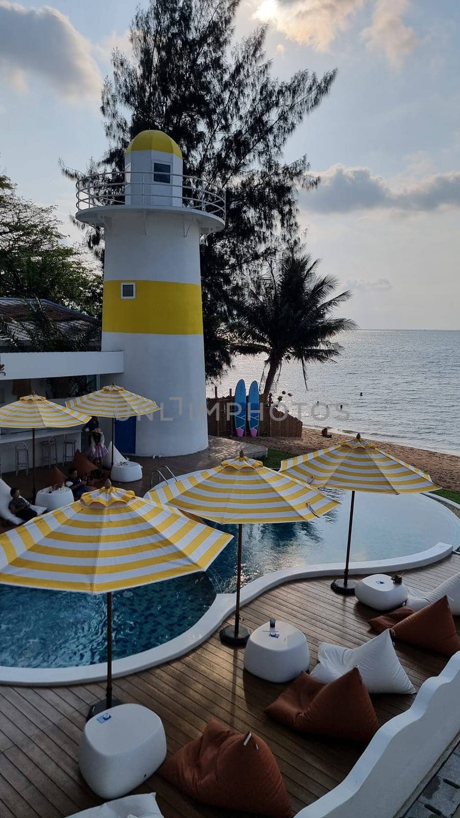 Bangsaray Pattaya Thailand 28 February 2024, Relax by the pool with colorful umbrellas, while gazing at the striking lighthouse in the distance against a clear blue sky.