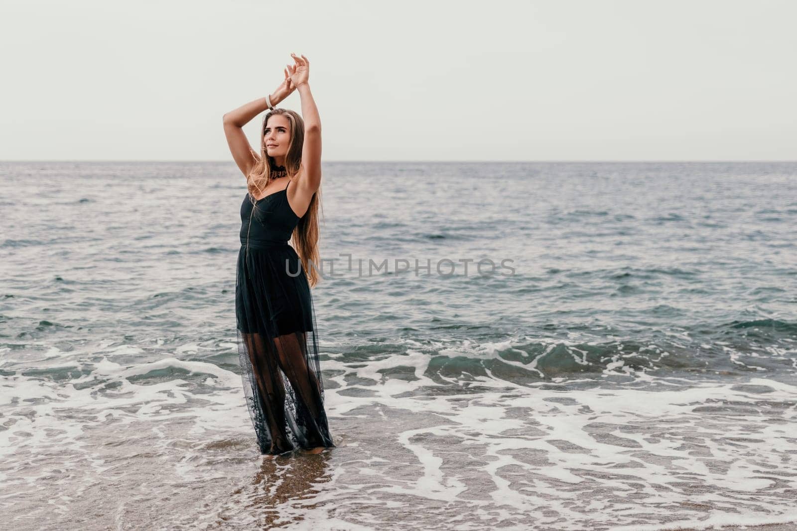 Woman summer travel sea. Happy tourist in black dress enjoy taking picture outdoors for memories. Woman traveler posing on sea beach surrounded by volcanic mountains, sharing travel adventure journey by panophotograph