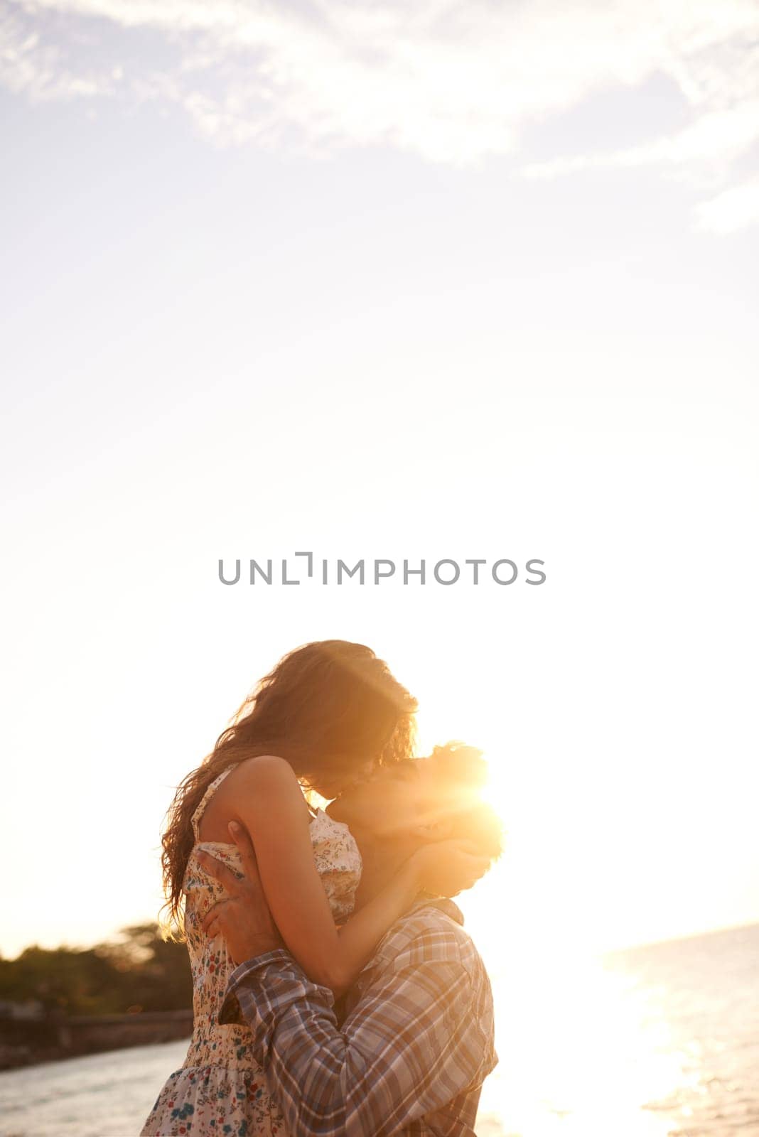 Couple, kiss at beach and travel with sunset, ocean and vacation in Cancun for date or anniversary for love. Affection, bonding and hug with people on adventure together, commitment and trust outdoor by YuriArcurs