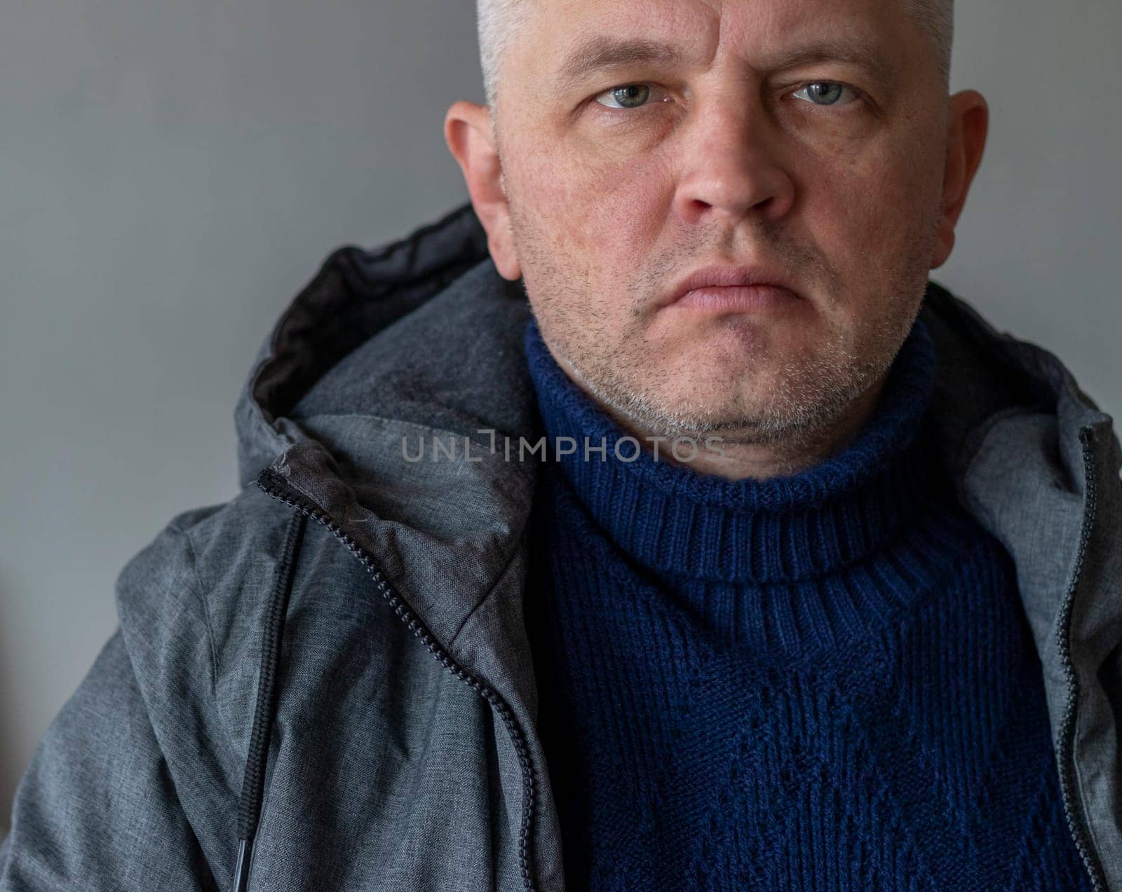 Portrait of the mid aged man with grey hair, wearing warm, dark blue sweater and grey coat.