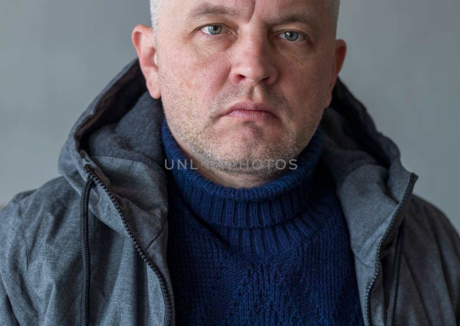 Portrait of the mid aged man with grey hair, wearing warm, dark blue sweater and grey coat.