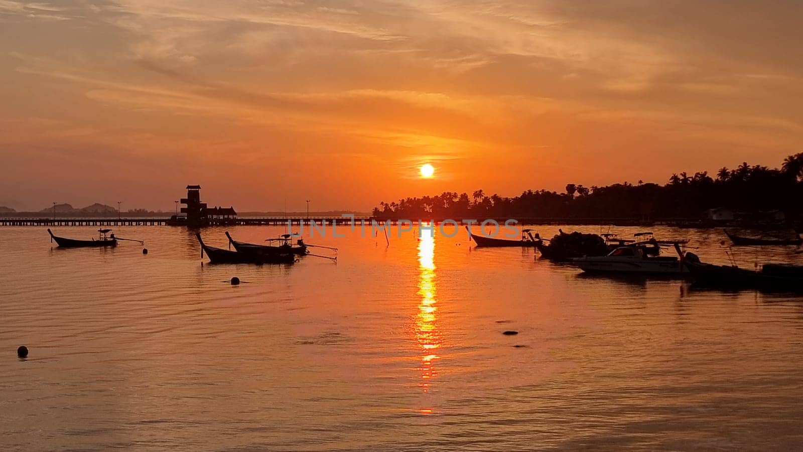 A picturesque scene of a group of longtail boats peacefully floating on the water under a sunrise sky. Koh Mook Thailand