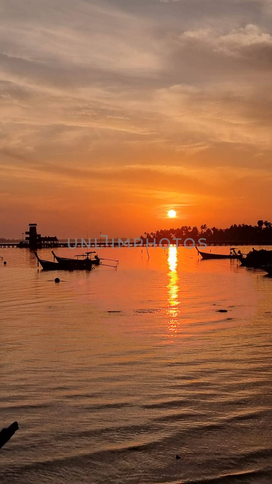 The sun sets over a tranquil body of water, casting a golden glow on the boats gently floating along. Koh Mook Thailand