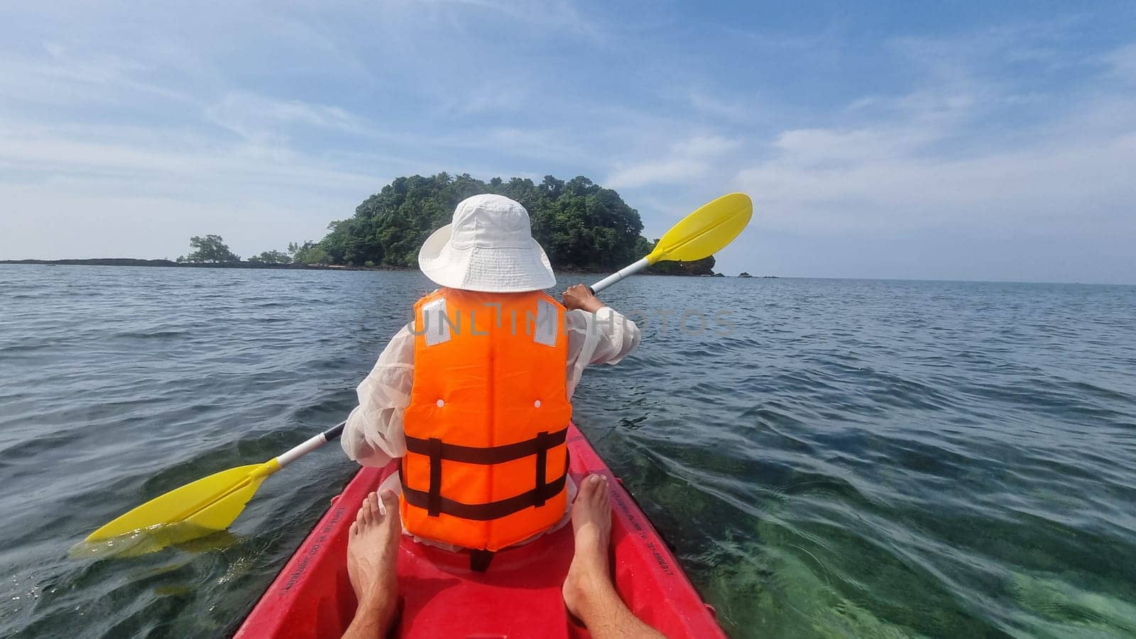 A person in a kayak paddling towards a small island in the distance under a clear blue sky on a calm day. women in kayak Koh Libong Thailand