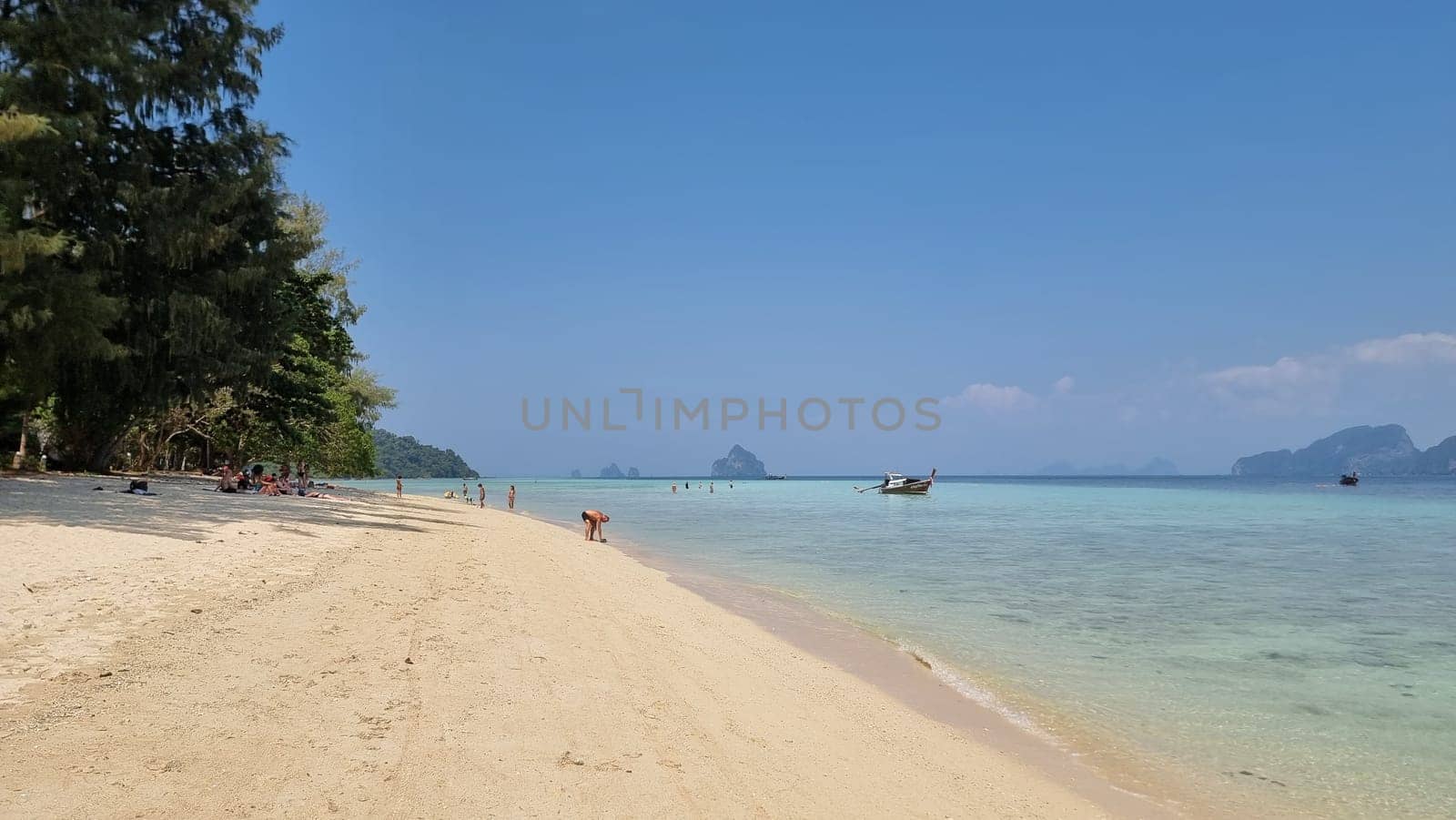 A tranquil sandy beach with a colorful boat peacefully floating in the crystal-clear water. Koh Kradan Thailand