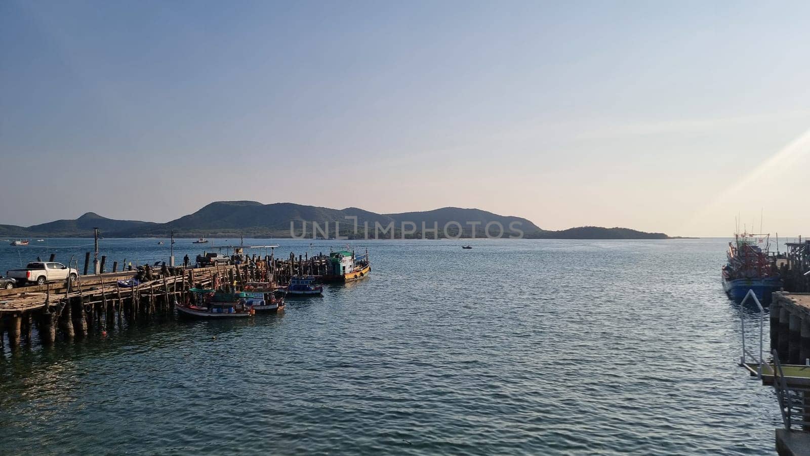 A vast body of water glimmers under the sun next to a weathered pier, where seagulls soar and the gentle waves lap against the wooden posts by fokkebok