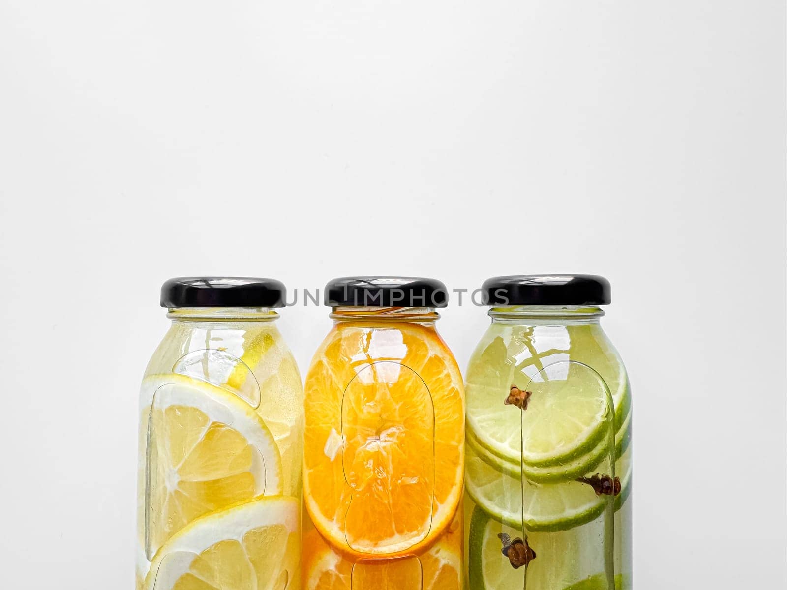 Lemon, orange, and lime detox drinks in glass bottles on white background with copy space. Concept for design and print. by Lunnica