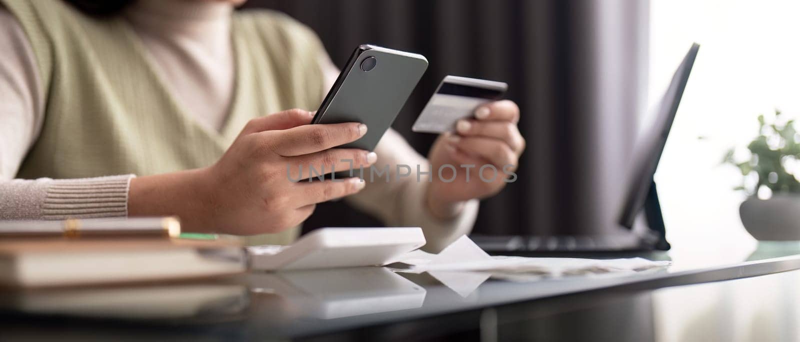 Young woman holding mobile phone and credit card sitting at the table. Happy woman makes online shopping using mobile payment. banking app service by nateemee