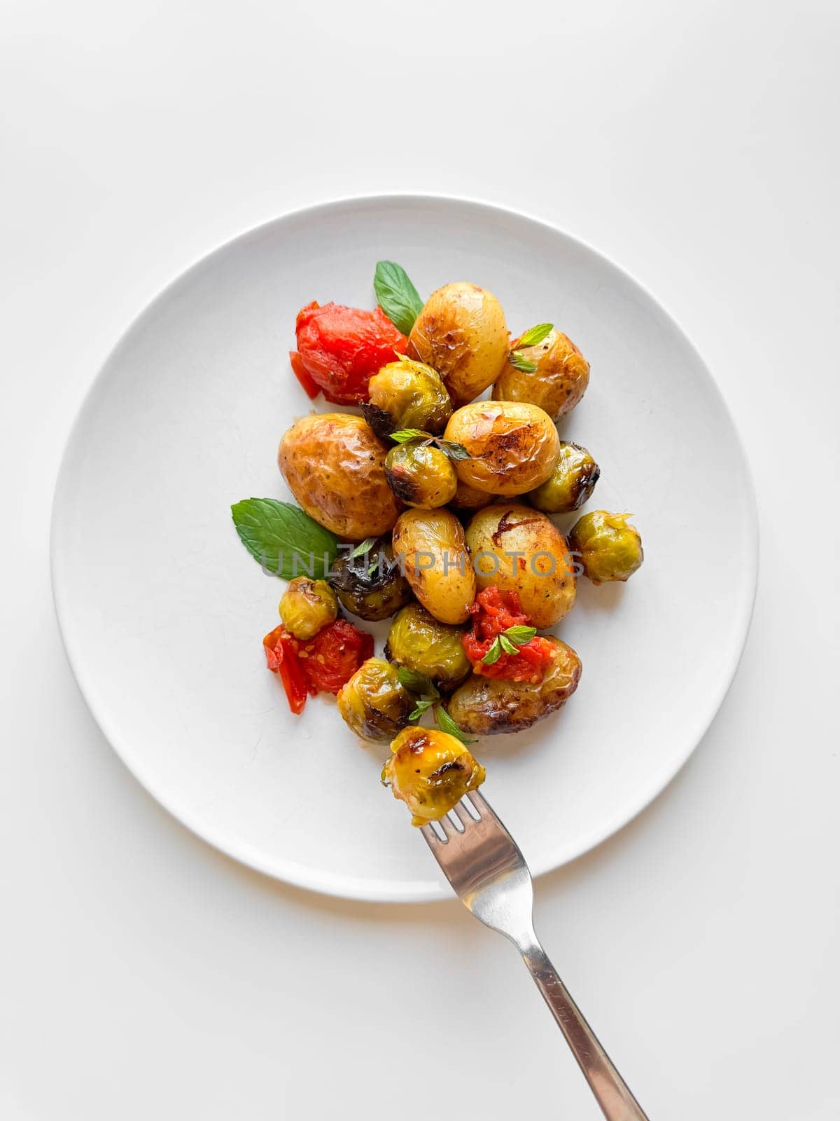 Roasted new potatoes and Brussels sprouts with cherry tomatoes and basil on white plate, healthy eating concept for weight loss. High quality photo