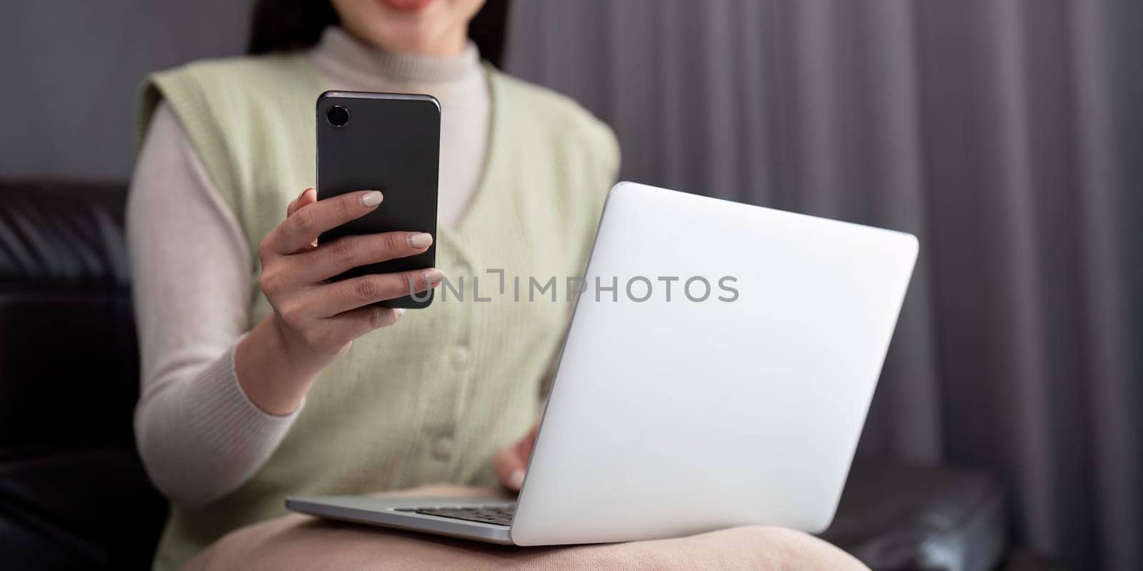 Young business woman using mobile phone, working on laptop computer at home. Female freelancer online working, using smartphone surfing the internet, remote work.