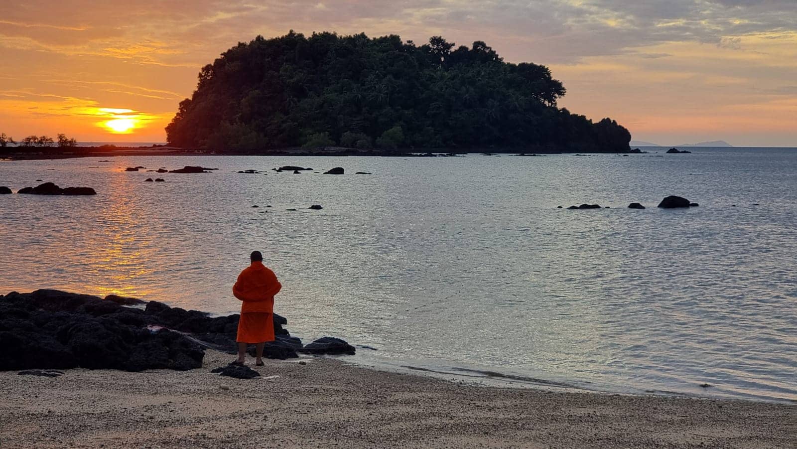 A solitary figure stands on a sandy beach as the sun sets, casting a warm glow over the horizon by fokkebok