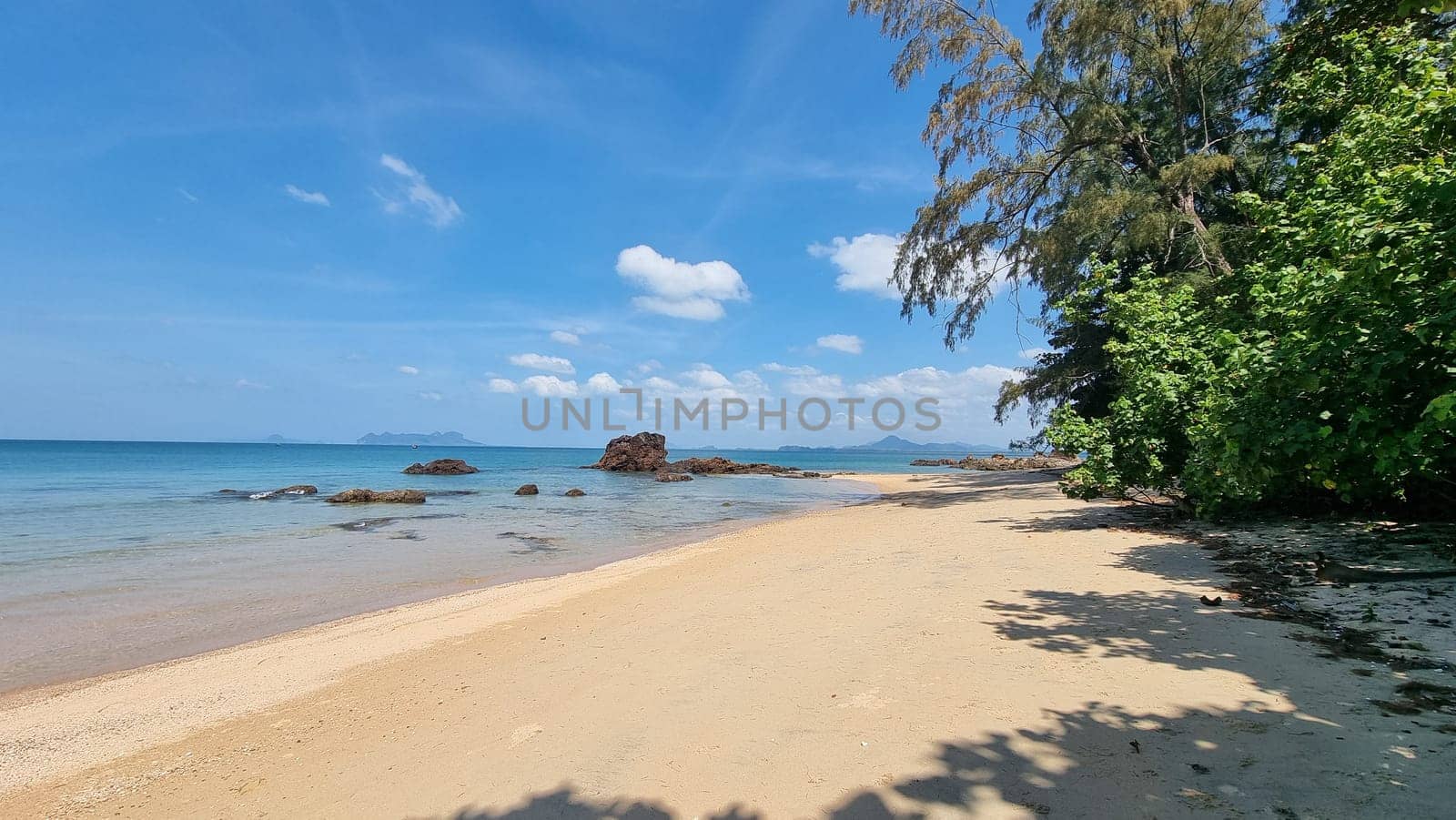 A sandy beach stretching out next to the sparkling ocean under a clear blue sky, creating a serene and picturesque scene by fokkebok