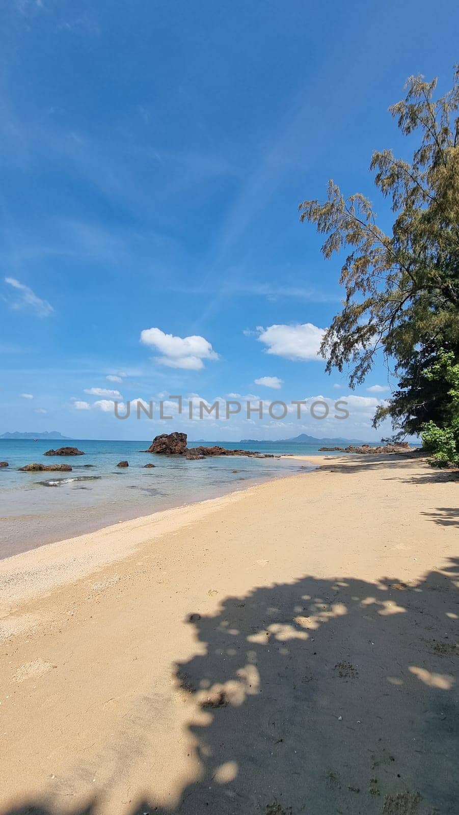 A tranquil sandy beach meets the vast ocean under a clear blue sky, creating a picturesque setting where waves gently kiss the shore.Koh Libong Thailand