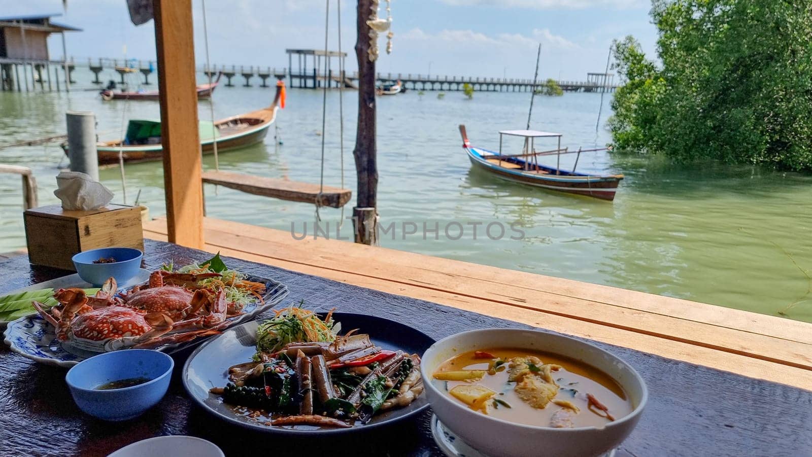 A well-set table adorned with various dishes, surrounded by the serene waters of a lake or ocean, creating a picturesque setting for a delicious meal. Koh Libong Thailand