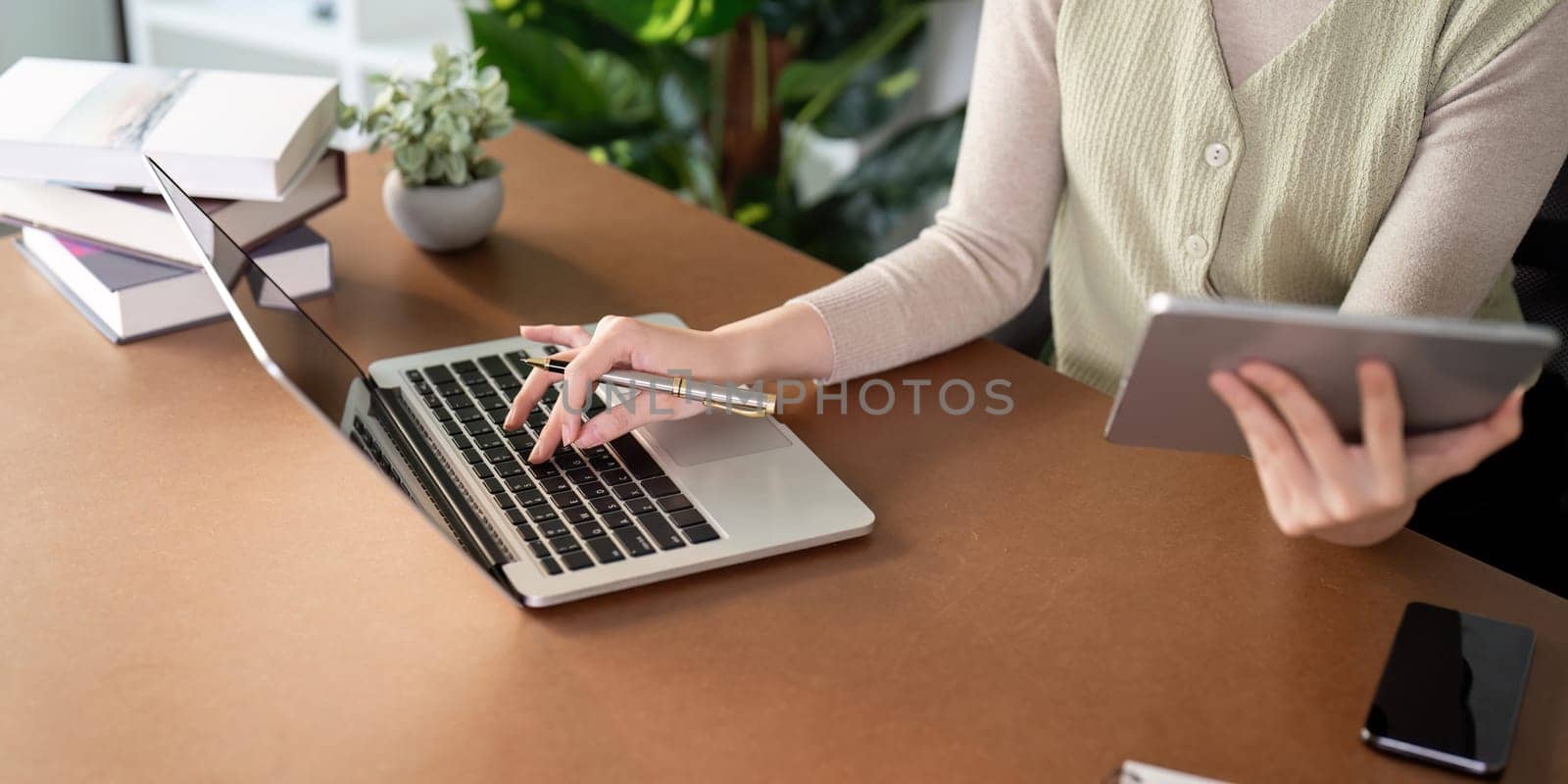Woman sitting at desk and working at computer laptop and tablet PC at home.