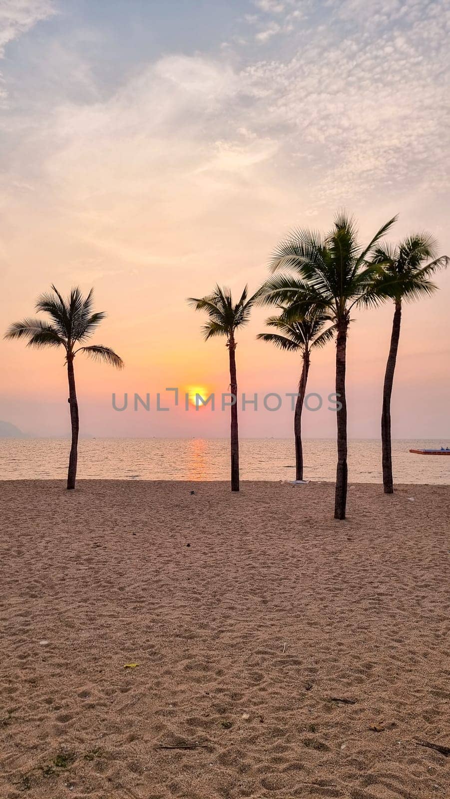 Palm trees sway gently in the breeze as a boat peacefully glides in the distance on the tranquil beach. Pattaya Thailand