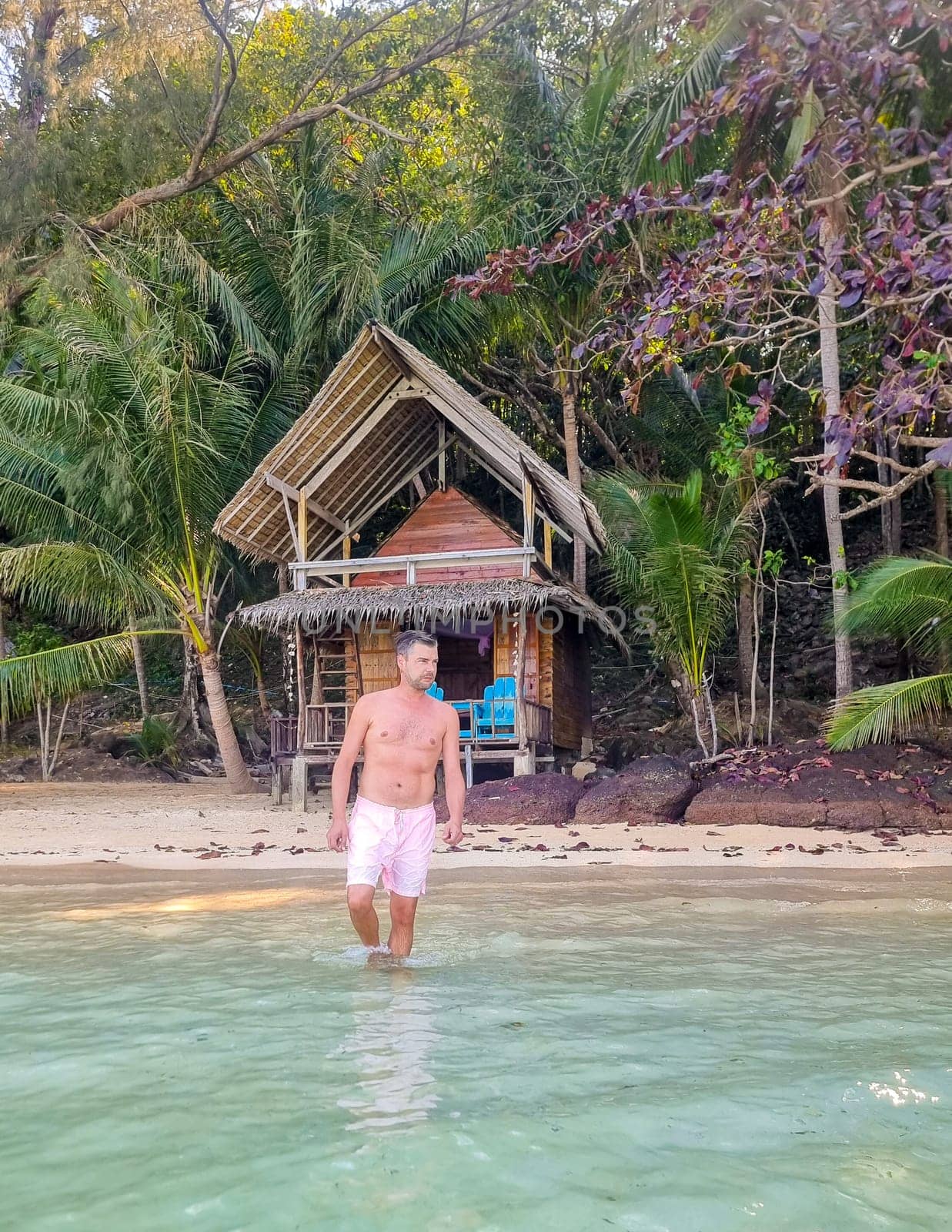 A man is peacefully standing in the water in front of a simple hut, surrounded by nature and tranquility. Koh Wai Thailand