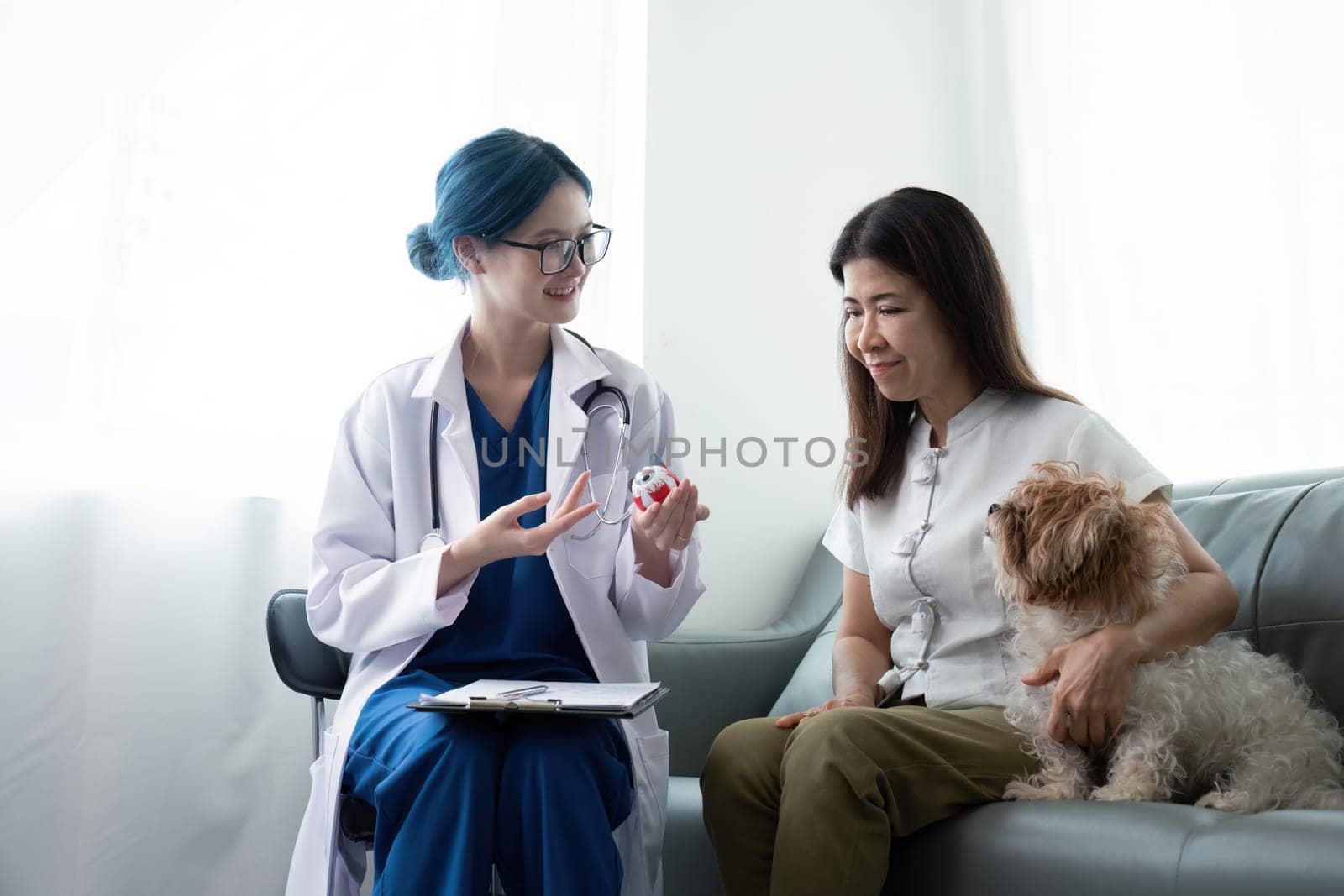Elderly woman with dog sitting by desk in front of asian woman veterinary at vet clinic.