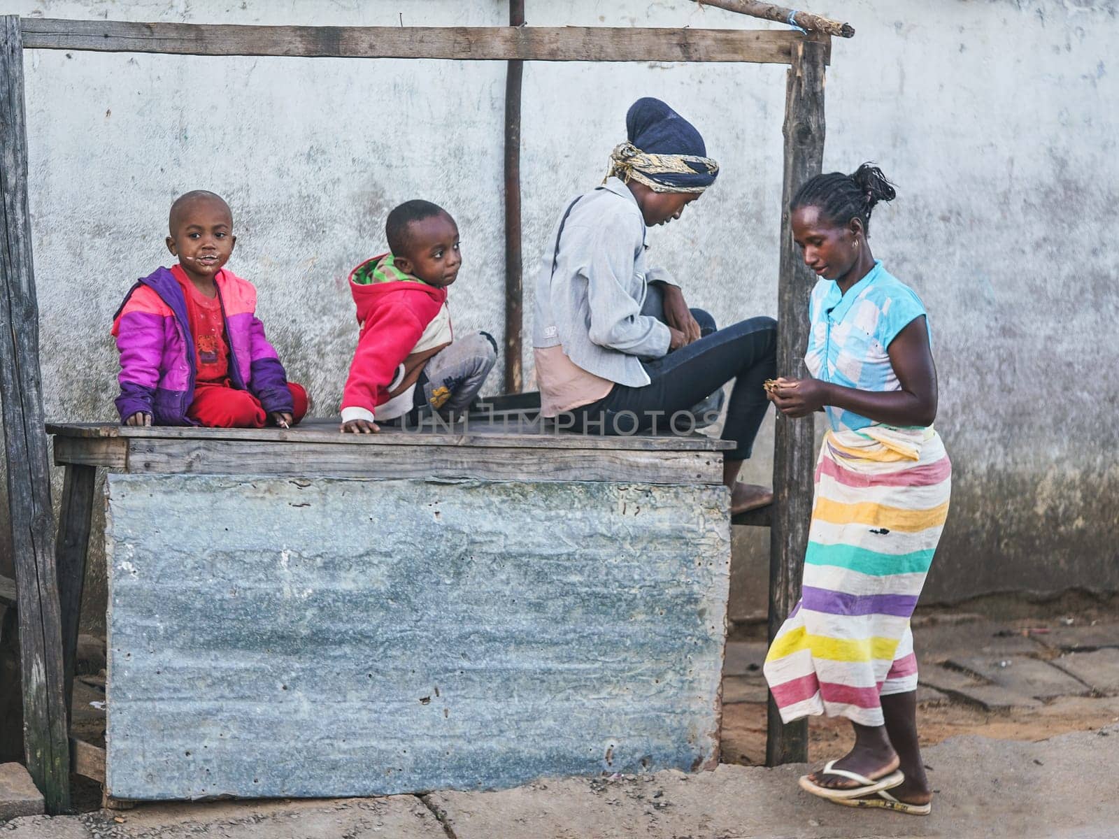 Ranohira, Madagascar - April 29, 2019: Four unknown Malagasy children playing next to unused wooden market stall, smallest sitting on top desk. Children in Madagascar are poor but cheerful by Ivanko