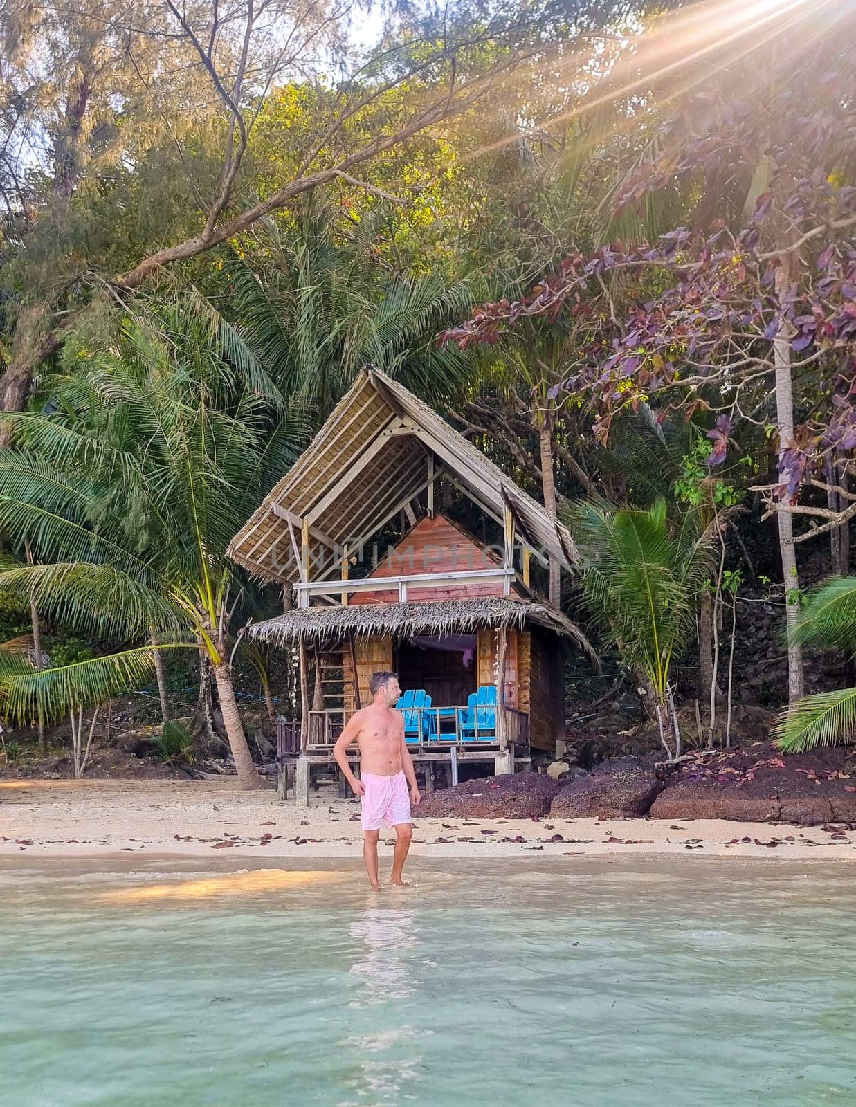 A man standing in the serene waters in front of a rustic hut, surrounded by nature and tranquility by fokkebok