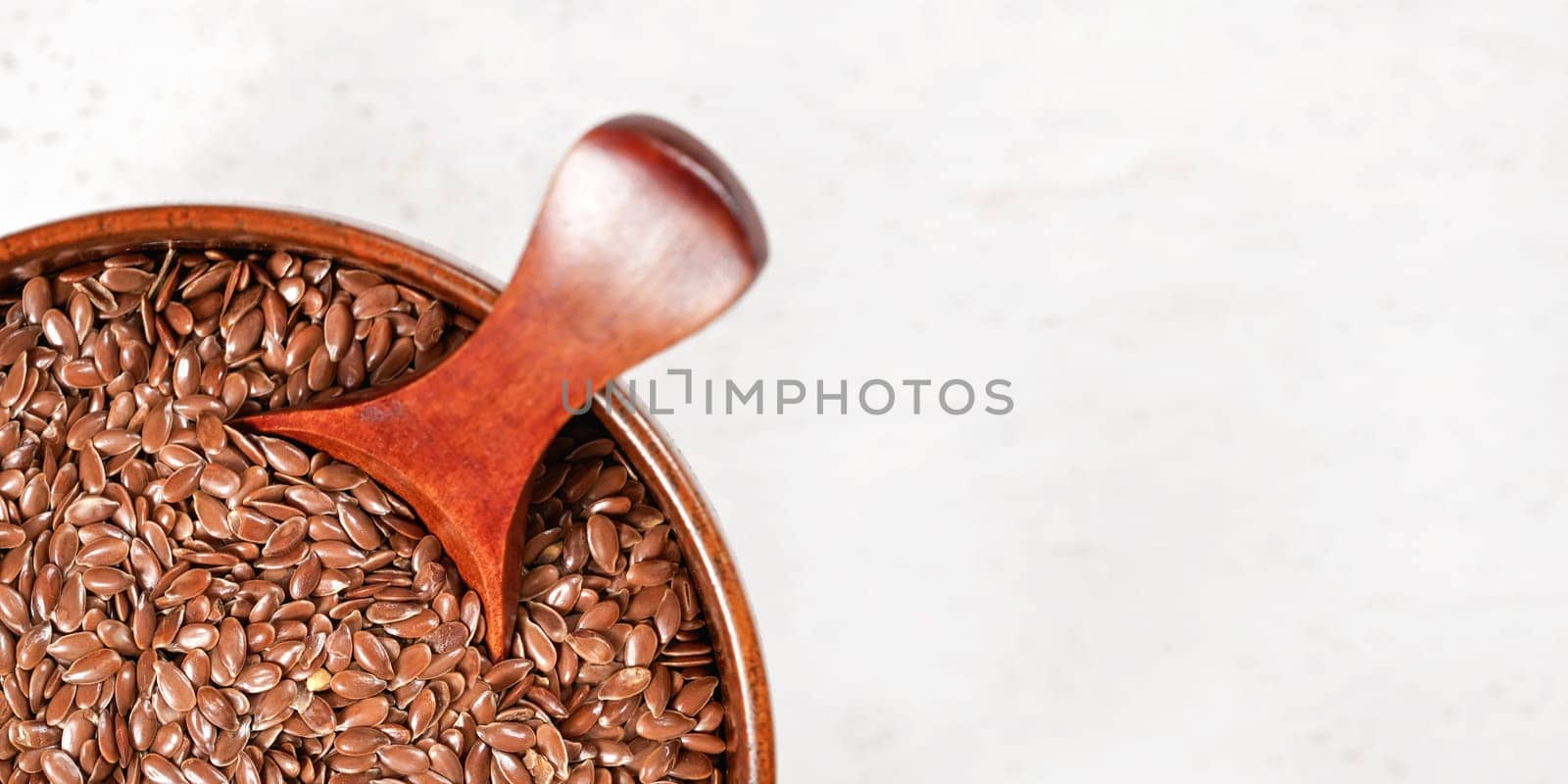 Small wooden bowl and scoop with common flax - Linum usitatissimum - seeds on white board, view from above, wide banner space for text right side by Ivanko