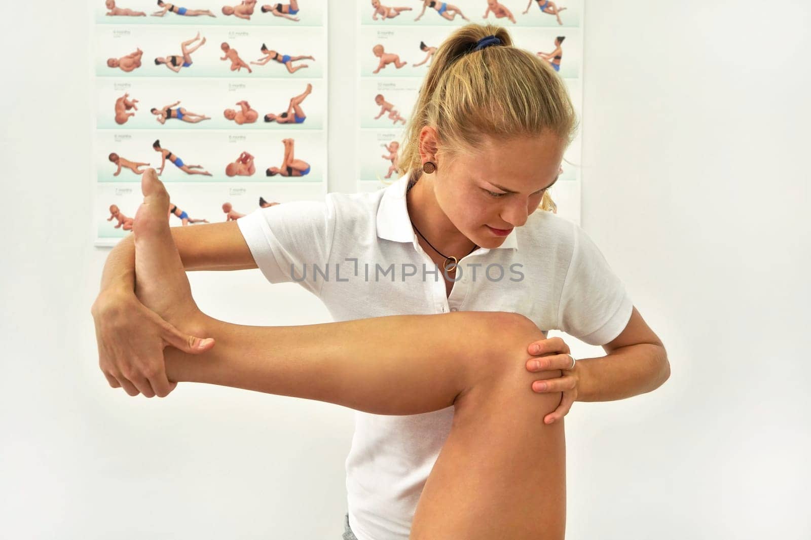 Young female physiotherapist exercising with her patient, flexing leg muscles while holding knee