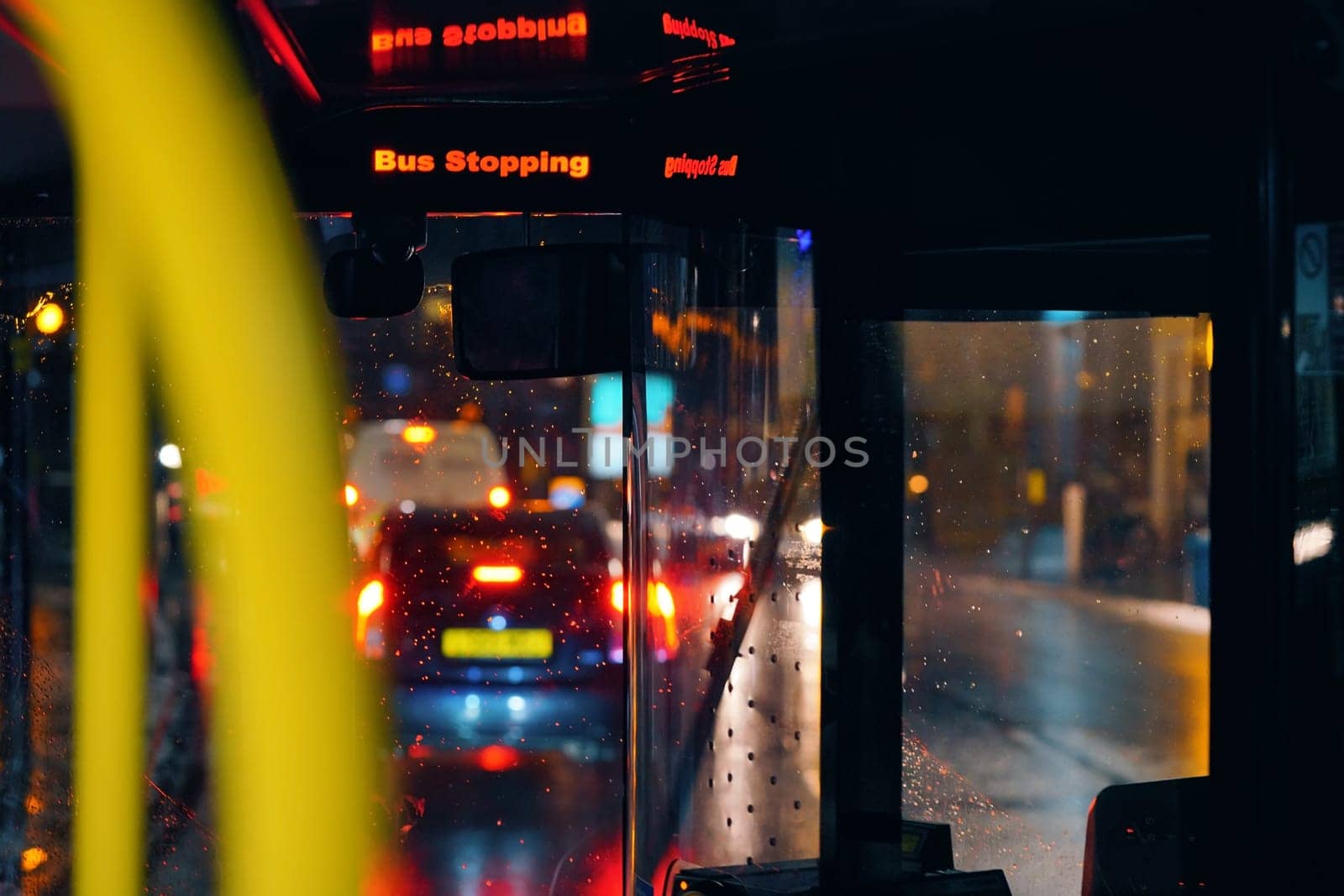 Bus stopping sign flashing in the public transport on rainy evening, blurred road and lights background by Ivanko