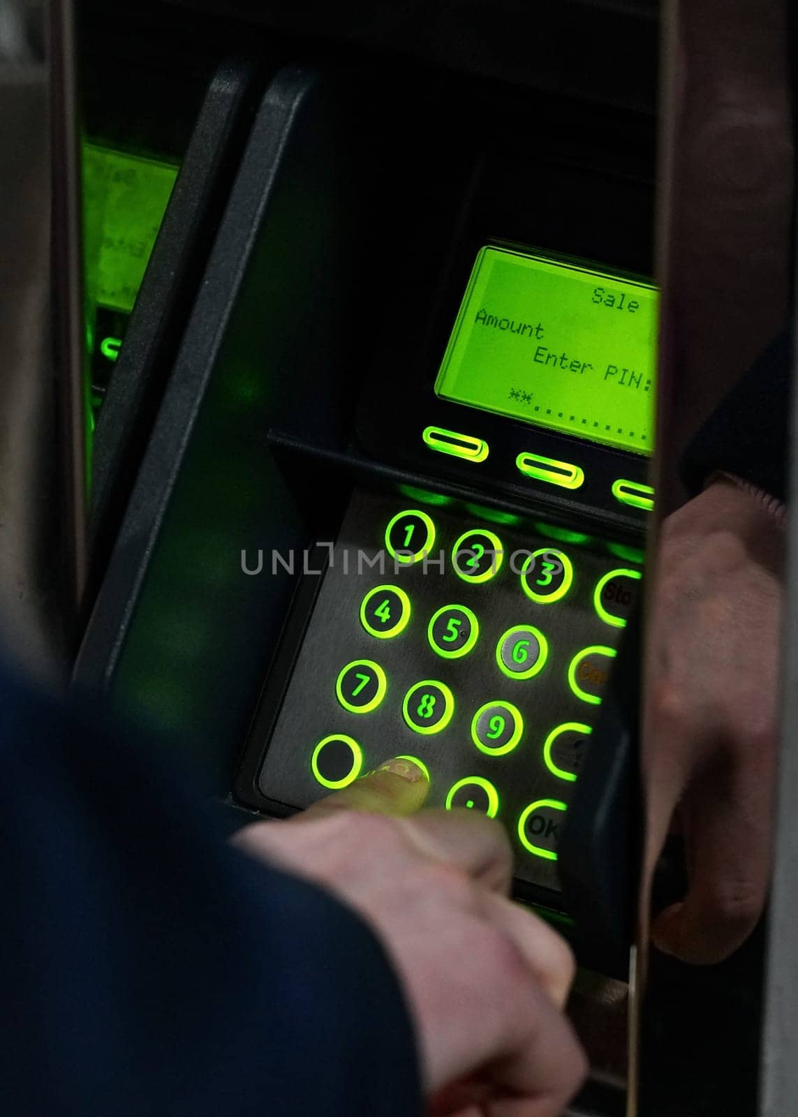 Man hand entering PIN on green illuminated atm machine keypad