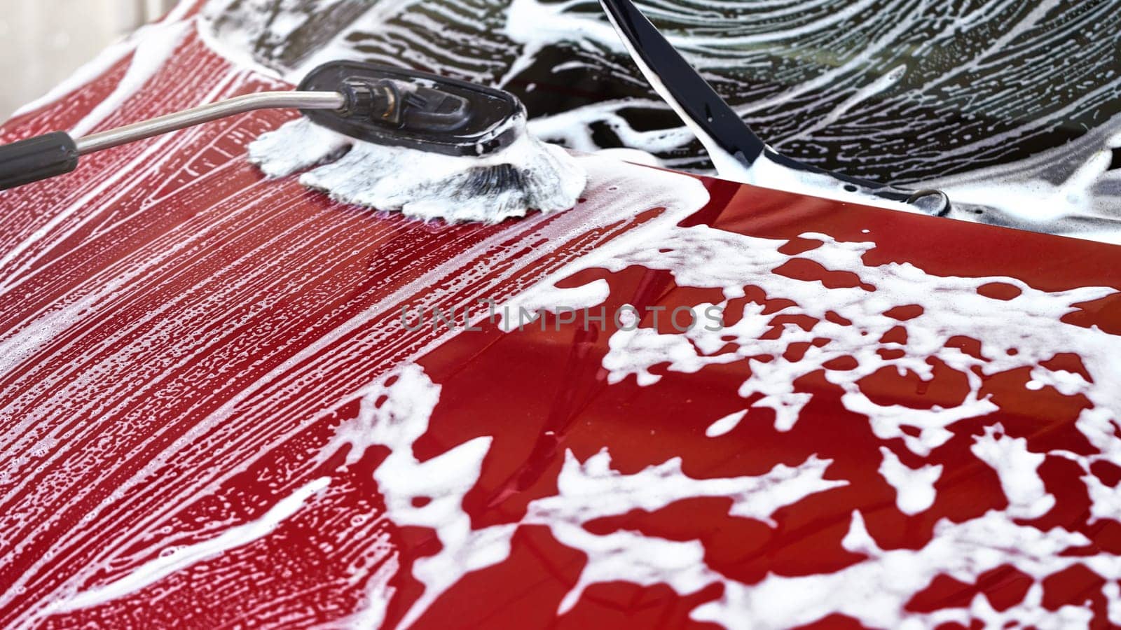 Red car washed in self serve carwash, detail on brush leaving white strokes on front hood by Ivanko