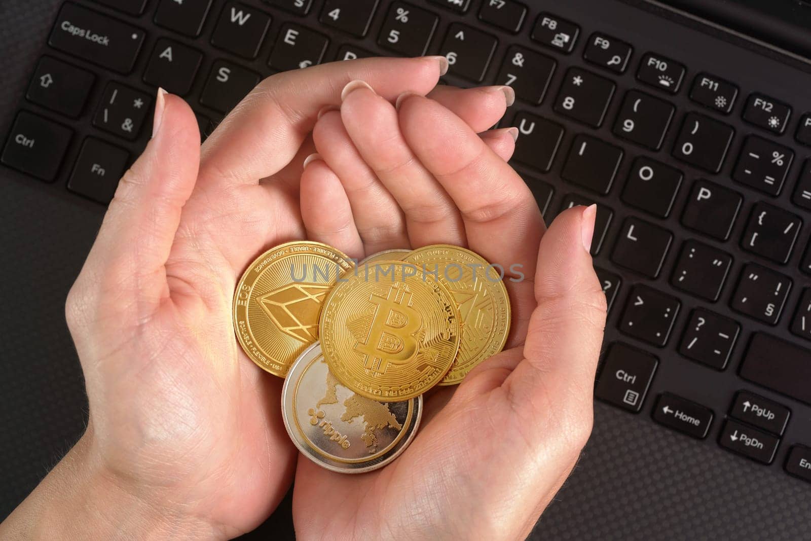 Woman holding golden coloured cryptocurrency coins in her hands over black laptop keyboard