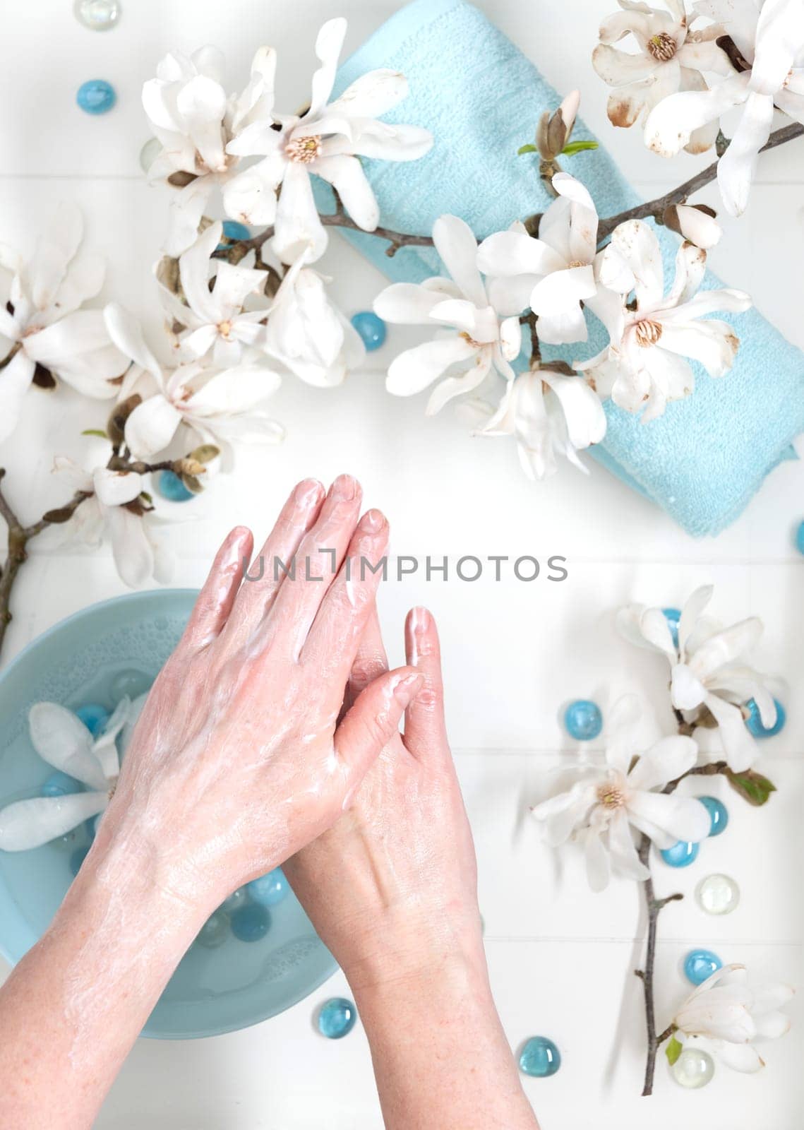 young woman doing step by step finger massage with cream in salon with cup of spring water and white magnolia flowers by KaterinaDalemans