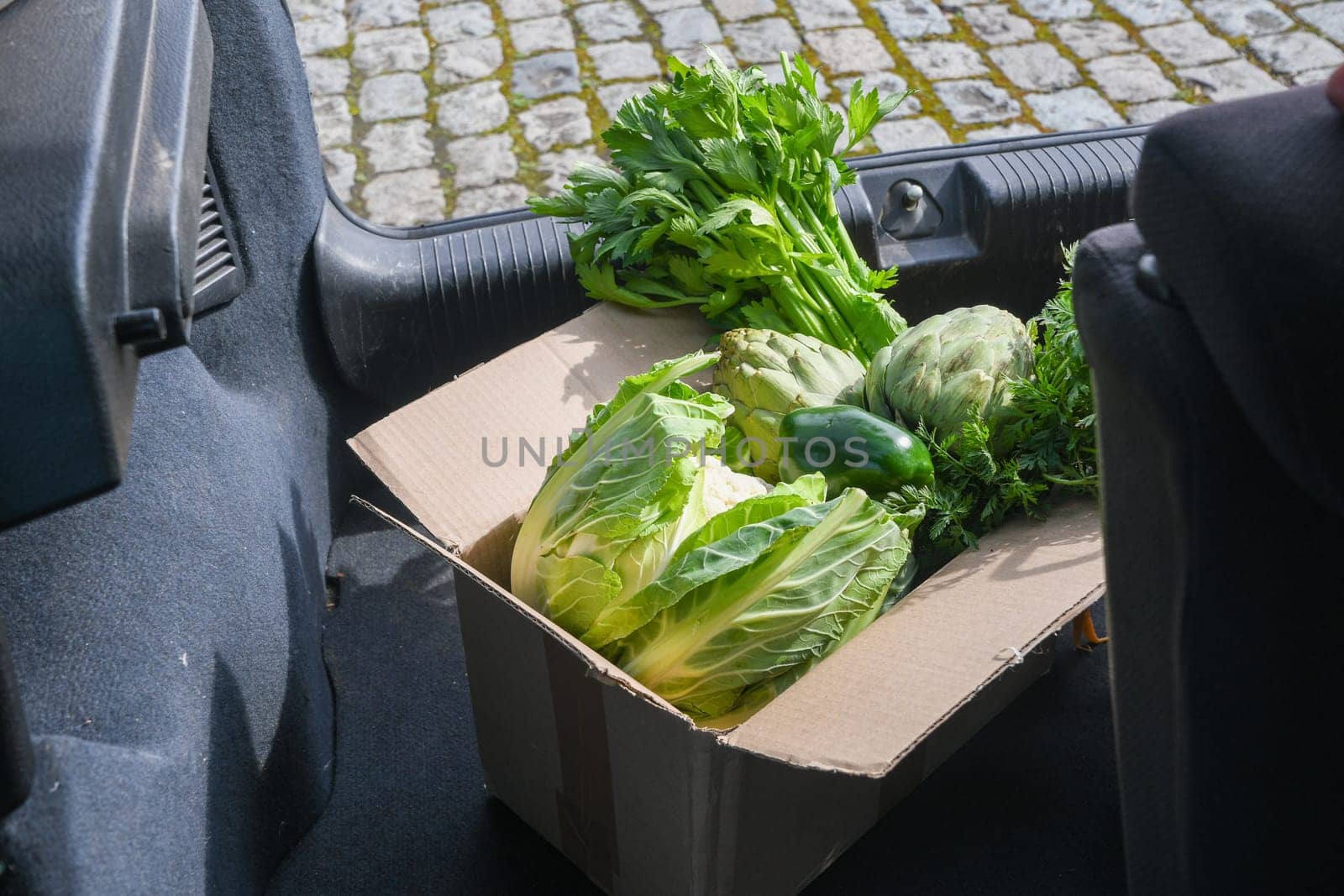 cardboard box with an assortment of fresh vegetables stands in the trunk of a car, natural products and healthy eating, the concept of cooking at home, high quality photo