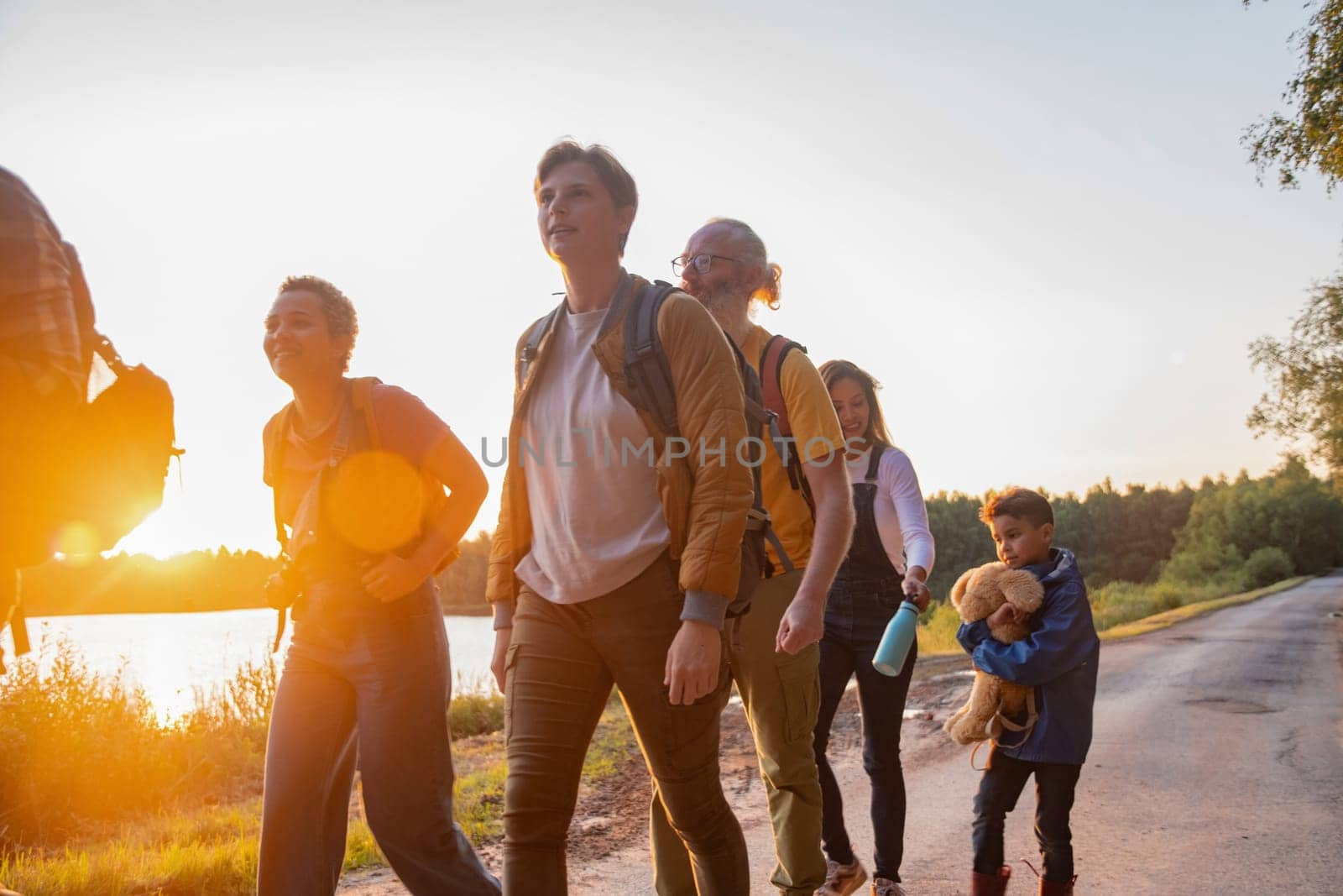 Large group of six family members of different ages and nationalities walks along a forest road against the backdrop of sunset,people walk with backpacks looking for picnic spot, high quality photo