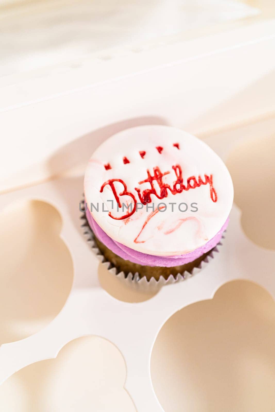 The birthday cupcakes, beautifully embellished with fondant decorations, are being carefully placed into white paper boxes, ready for their grand presentation.