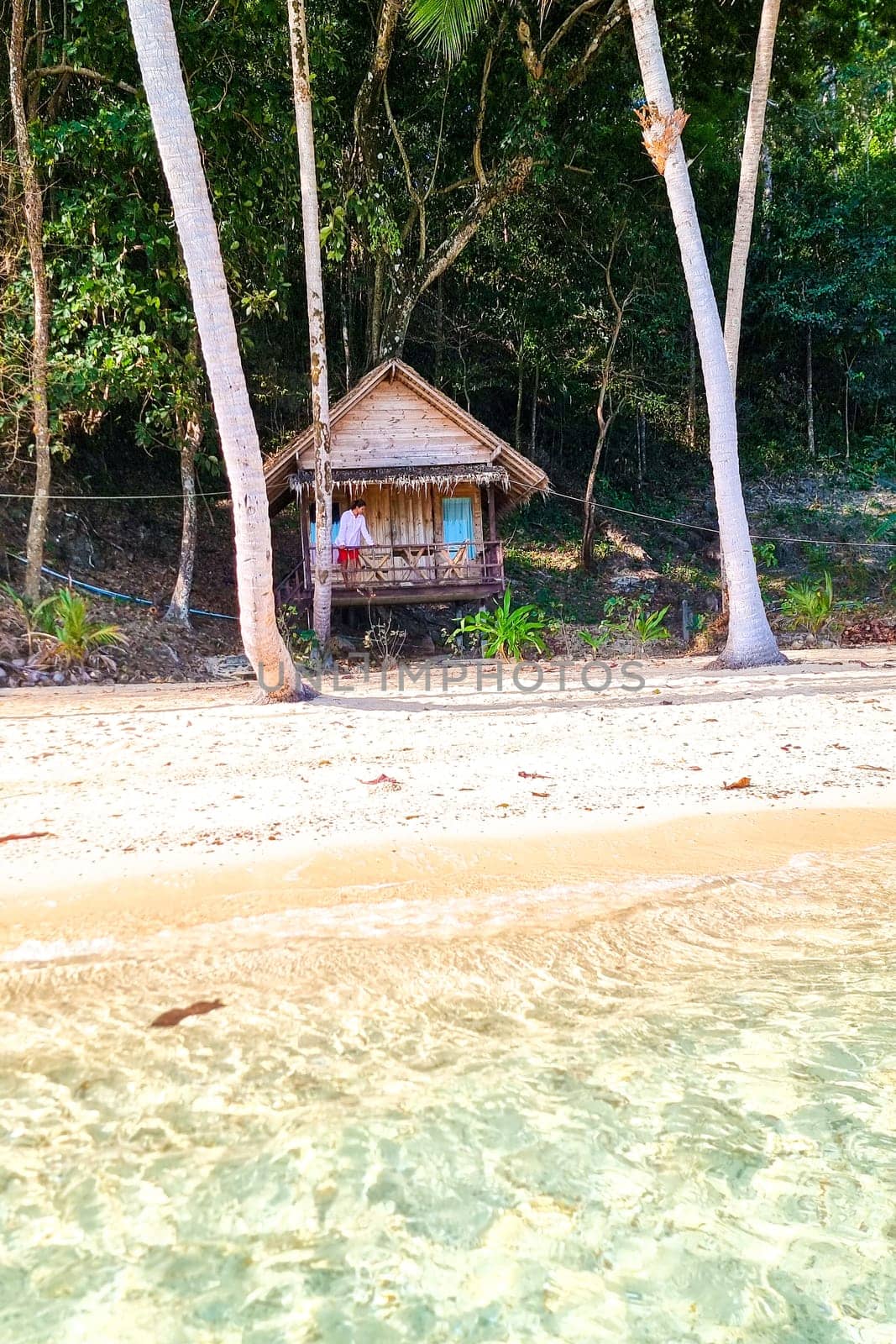 A traditional wooden hut nestled on the sandy shore of a pristine tropical beach, with lush palm trees swaying in the gentle breeze under a clear blue sky.