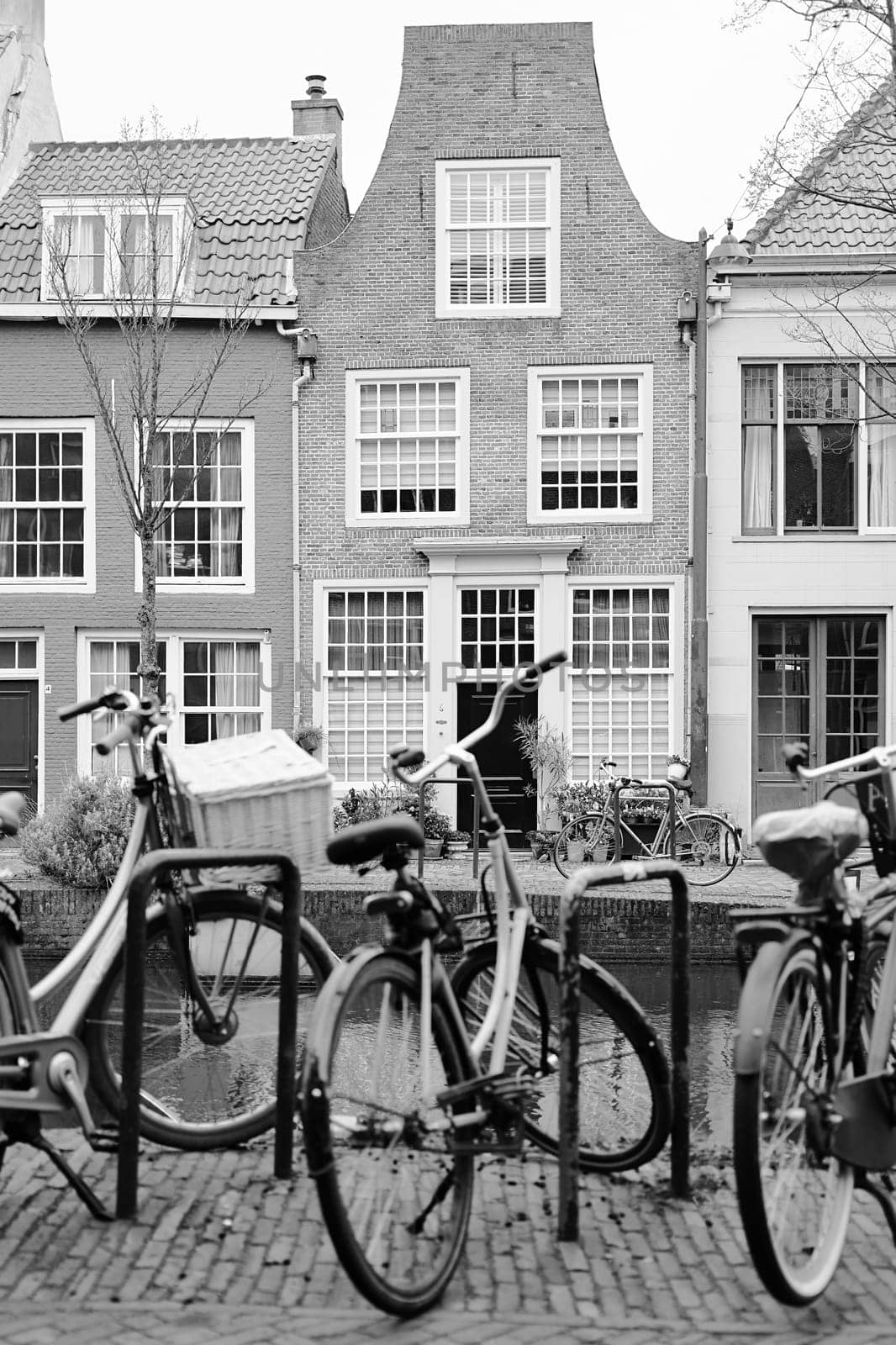 Picturesque Netherlands in black and white. Bicycles parked alongside a channel on beautiful old buildings background. by berezko