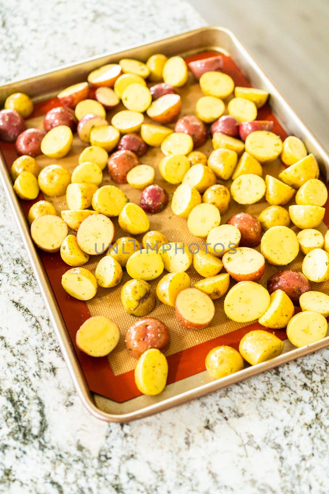 In a modern kitchen, an array of halved, multicolored marble potatoes are arranged on a baking pan lined with a silicone liner. The roasting process infuses the kitchen with a mouthwatering aroma, indicating a delicious side dish in the making.