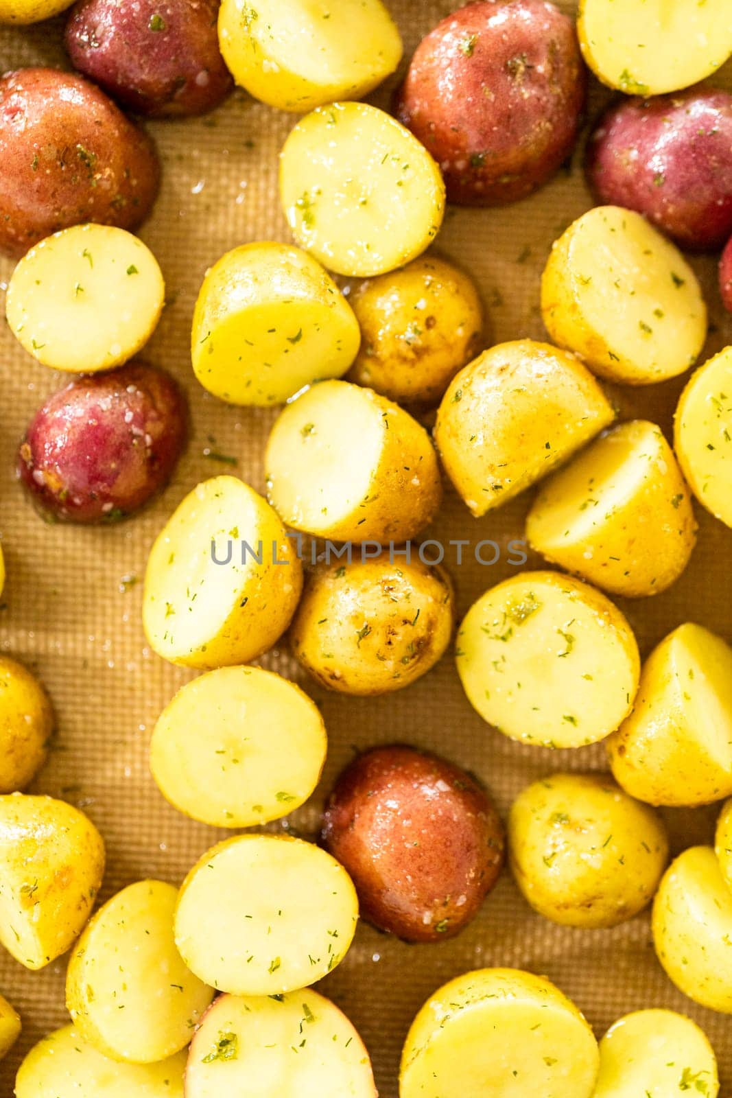 In a modern kitchen, an array of halved, multicolored marble potatoes are arranged on a baking pan lined with a silicone liner. The roasting process infuses the kitchen with a mouthwatering aroma, indicating a delicious side dish in the making.