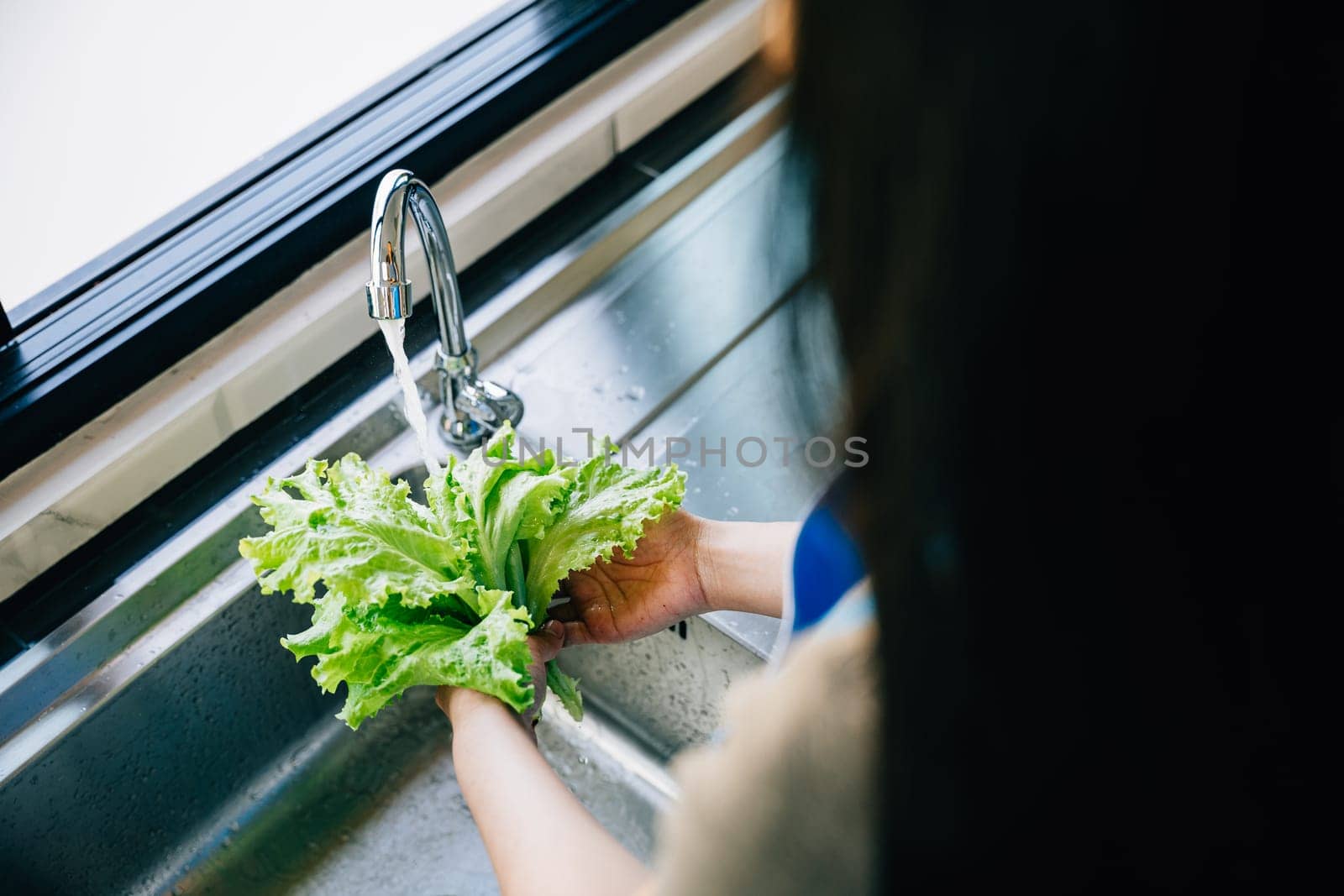 A woman's hands washing fresh vegetables under running water in a modern kitchen sink for a vegan salad preparation. Emphasizing hygiene and clean eating habits at home.