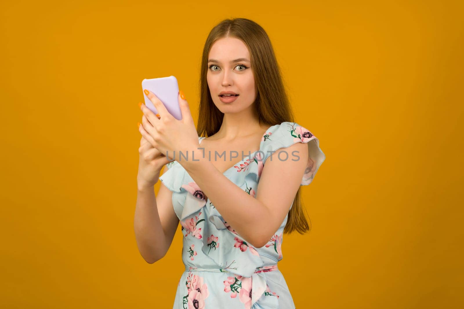 Young woman wears in sunner dress with flowers surprised by the news on a smartphone - image