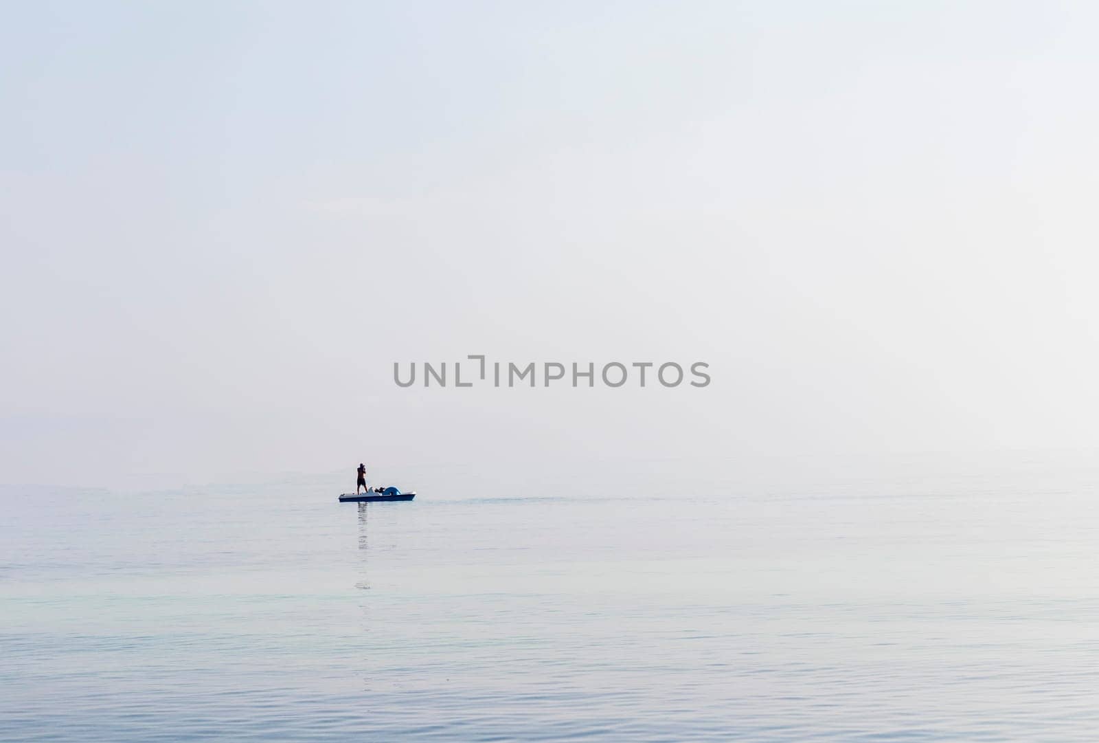 Shot of a man on a small catamaran boat by the horizon, which is hard to detect because of the fog and humidity