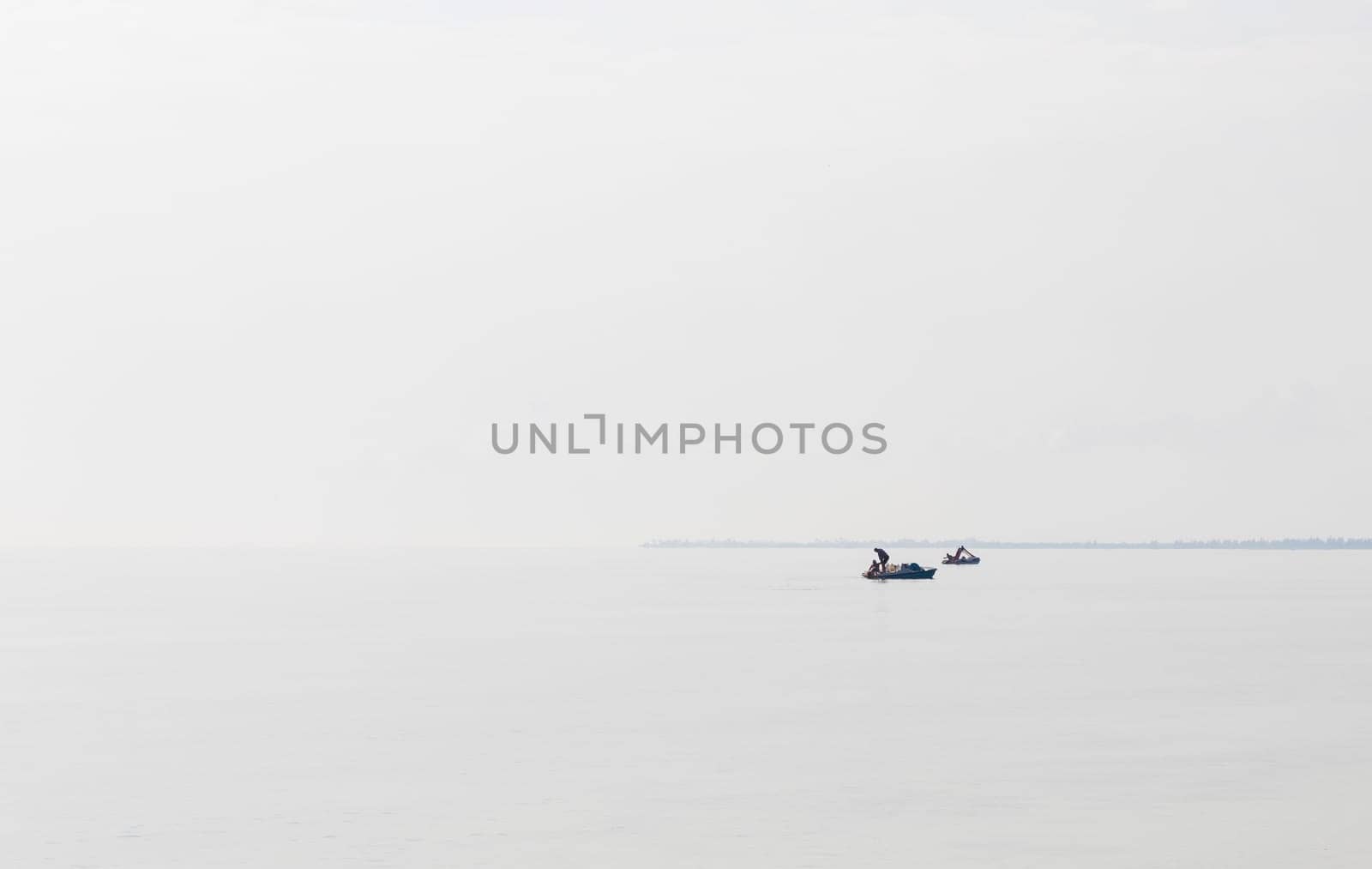 Shot of a man on a small catamaran boat by the horizon, which is hard to detect because of the fog and humidity